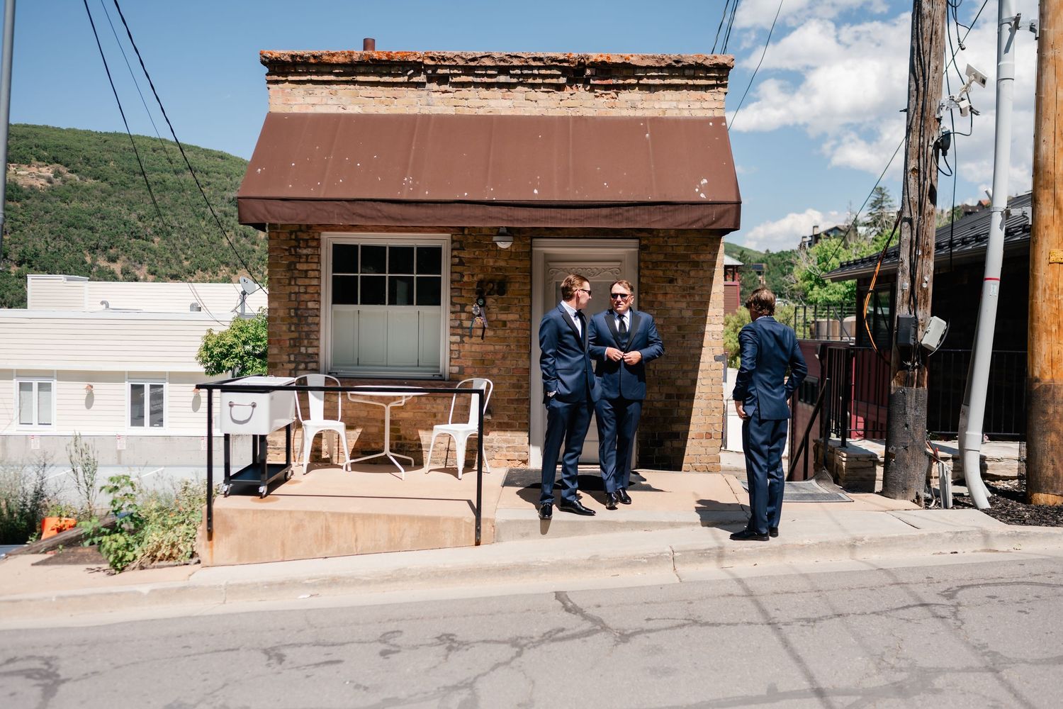 Small brick building with people gathered outside on a sunny mountain street.
