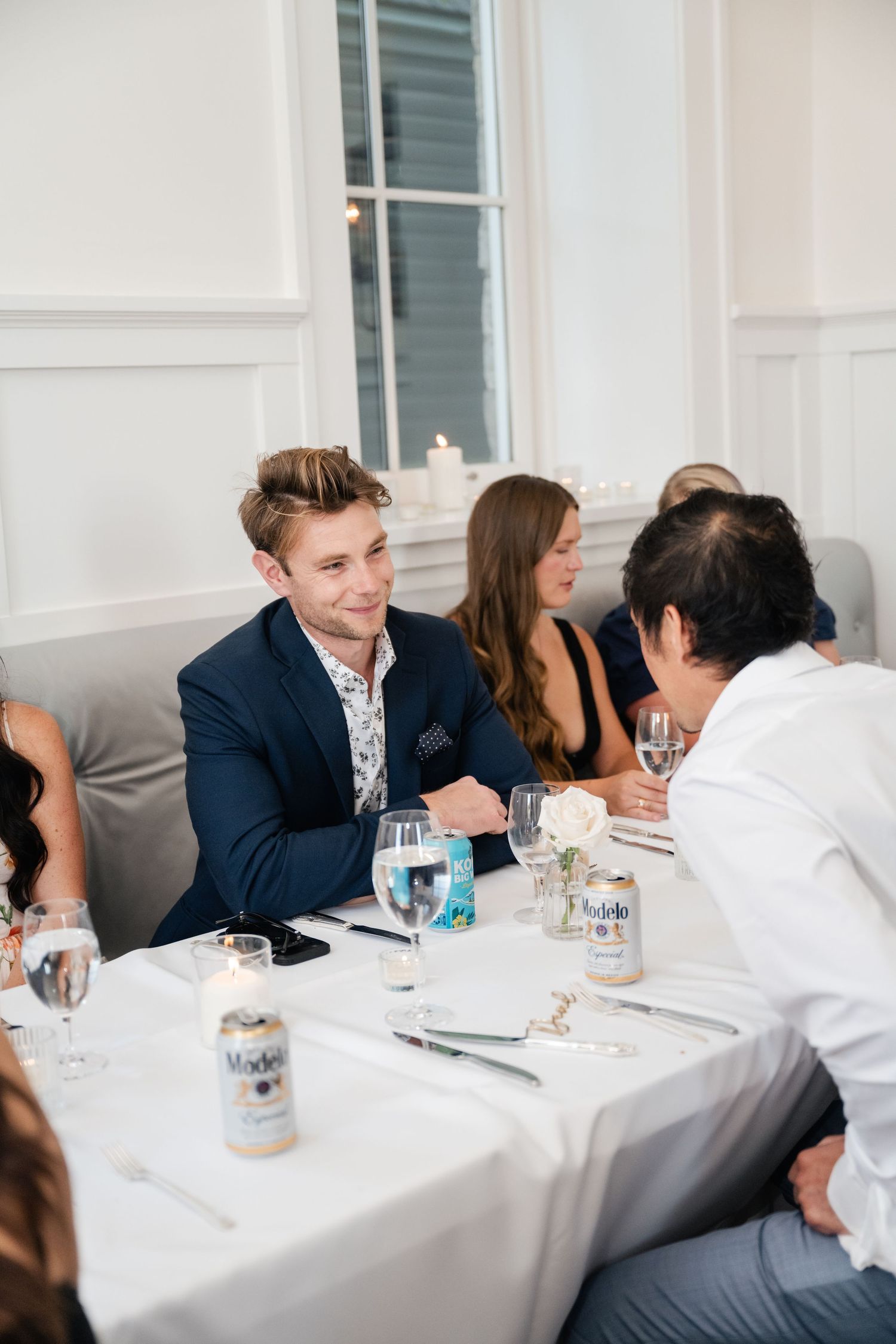Wedding reception guests seated at tables with white linens engage in lively conversation.