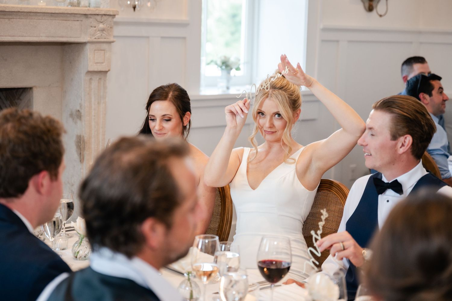 Wedding reception guests celebrate with animated expressions during indoor dinner party.