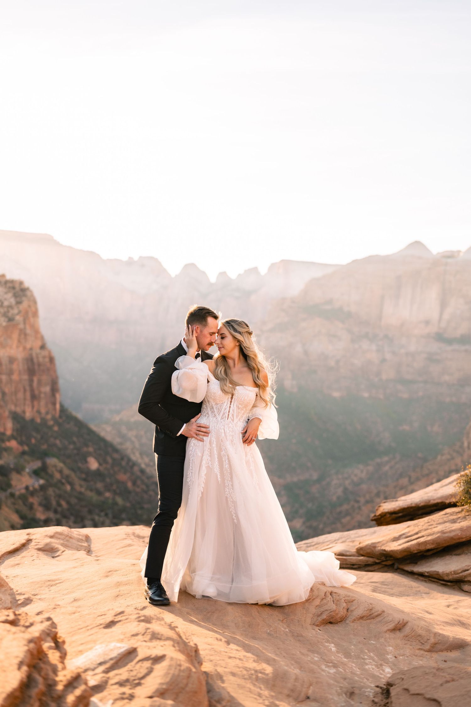 A couple shares an intimate moment at sunset overlooking a scenic canyon landscape. Zion wedding photographer.