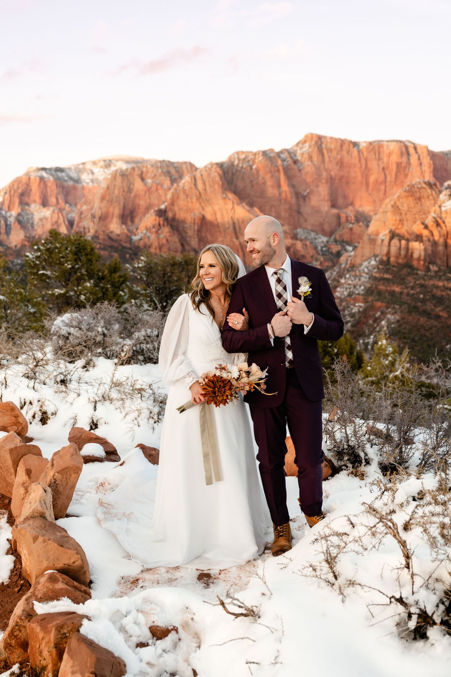 Winter wedding portraits with snow-covered landscape and red rock cliffs at sunset.