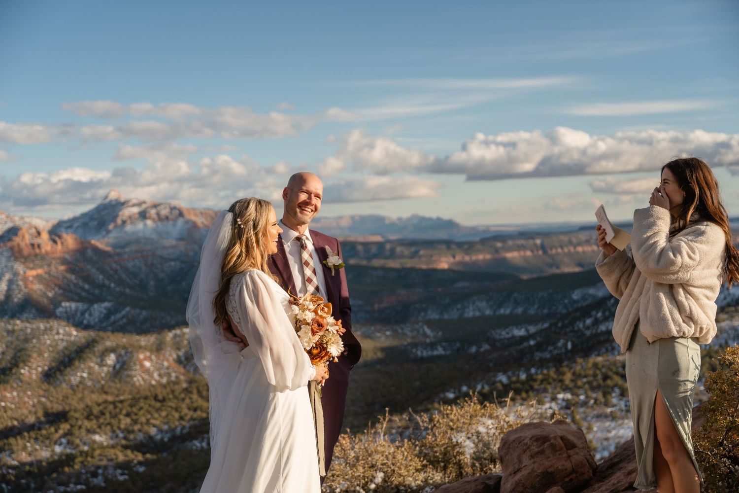 Scenic mountain landscape with red rock formations and snow against a bright blue sky.