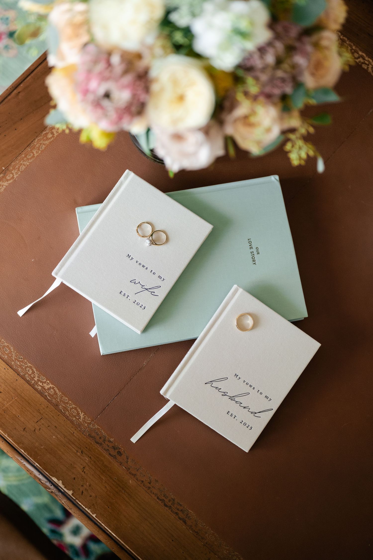 Wedding invitation cards and rings arranged with soft pink and white floral decorations on a wooden table.
