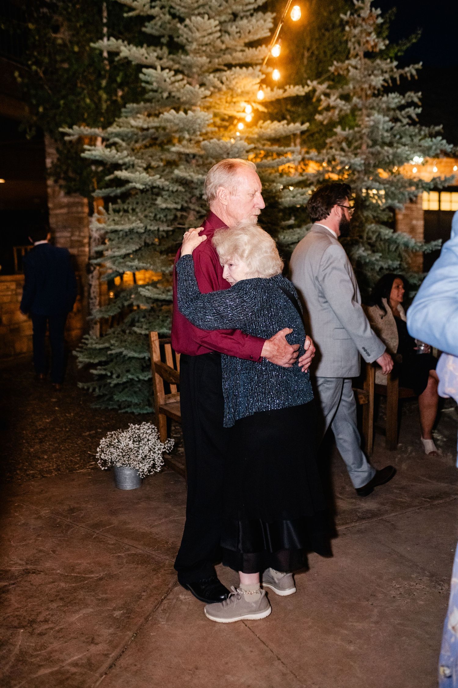 Wedding guests dance together under string lights at an evening outdoor reception.