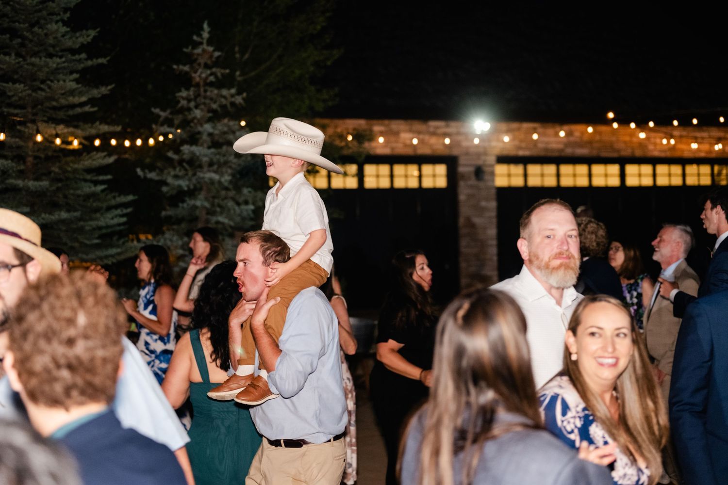 Wedding guests dance together on an outdoor dance floor under string lights at a nighttime reception celebration.