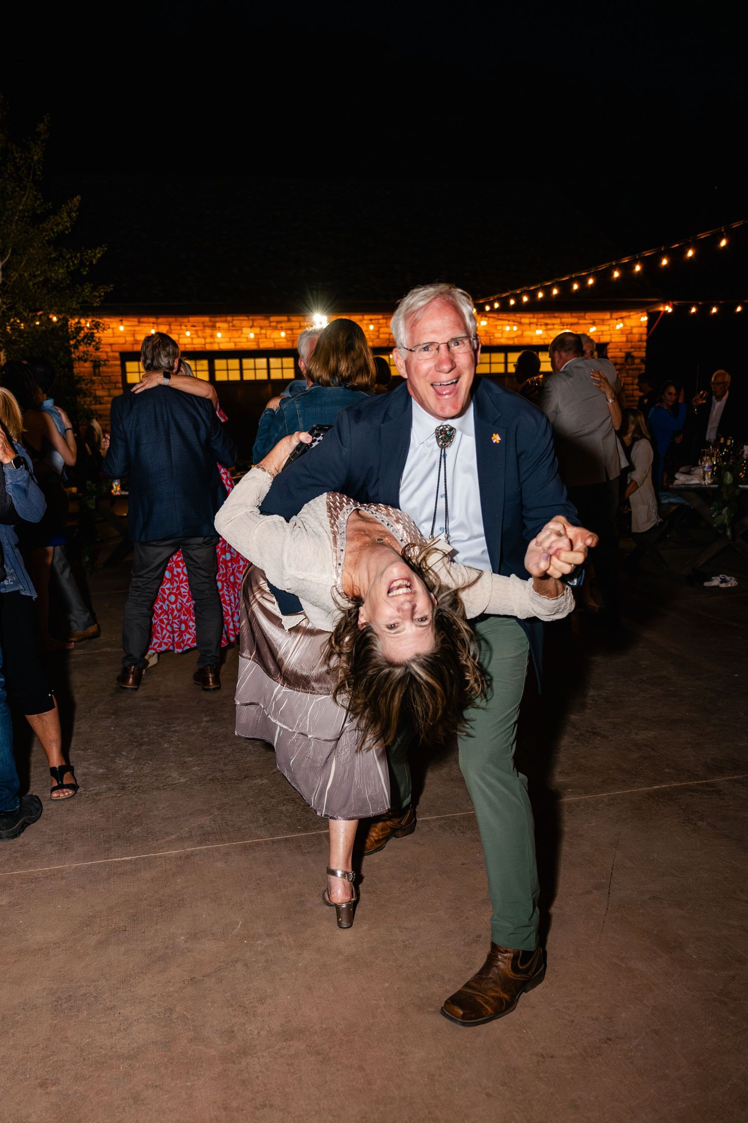 Couples dancing and dipping on an outdoor dance floor at night under string lights.