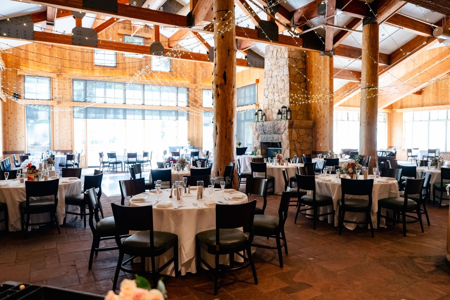 Elegant rustic wedding reception venue with exposed wooden beams, white tablecloths, and natural lighting.