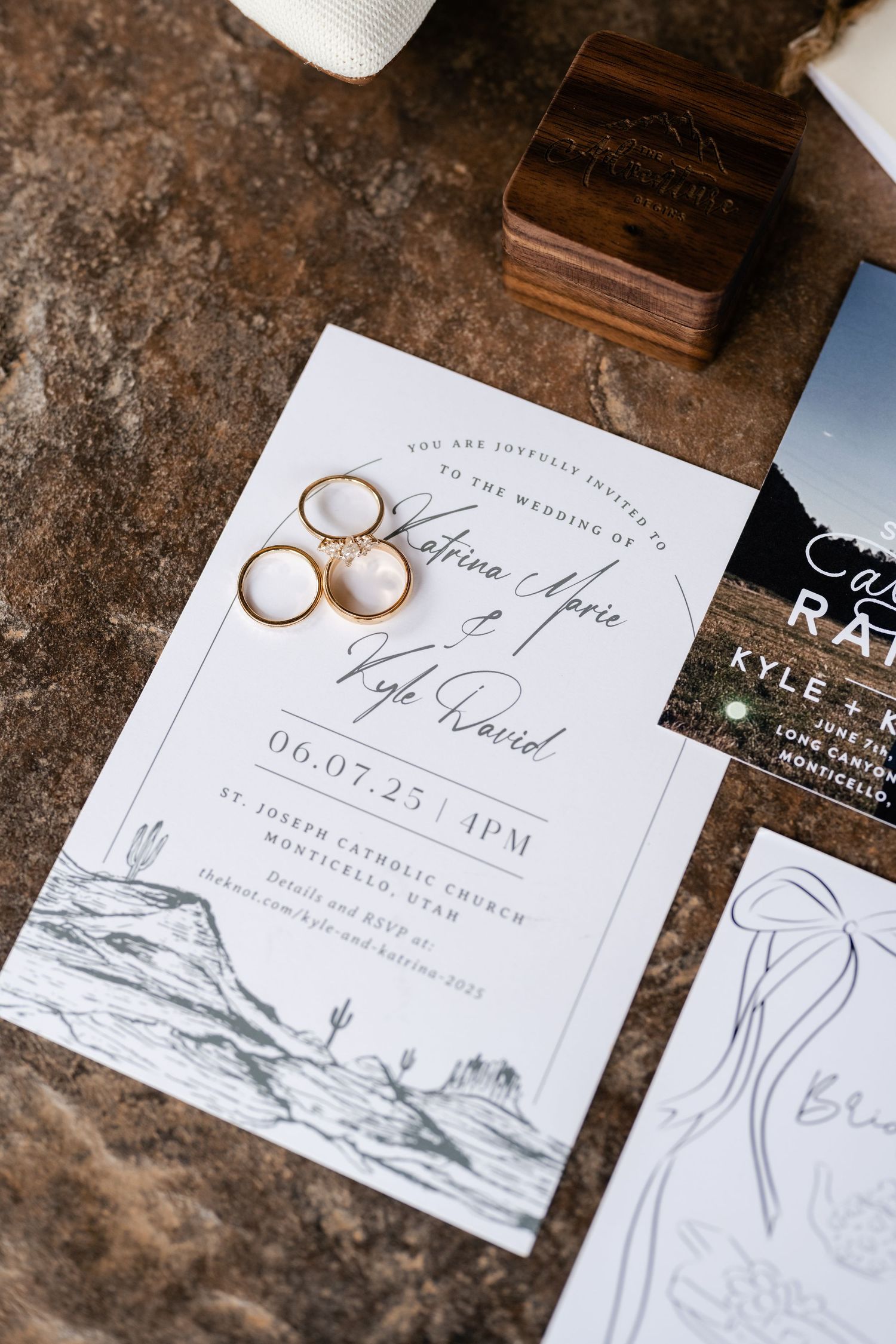 Wedding invitation and rings arranged on textured stone surface with elegant typography.