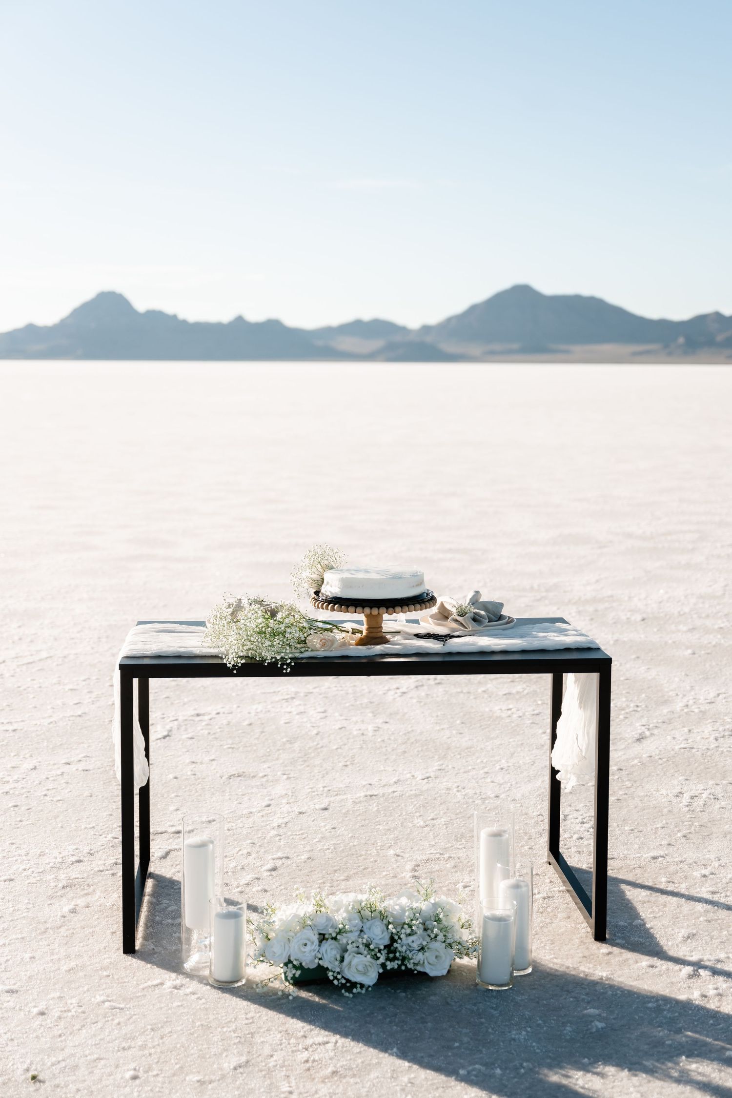 A minimalist table setting on the Bonneville Salt Flats with white decor and mountains in the background.