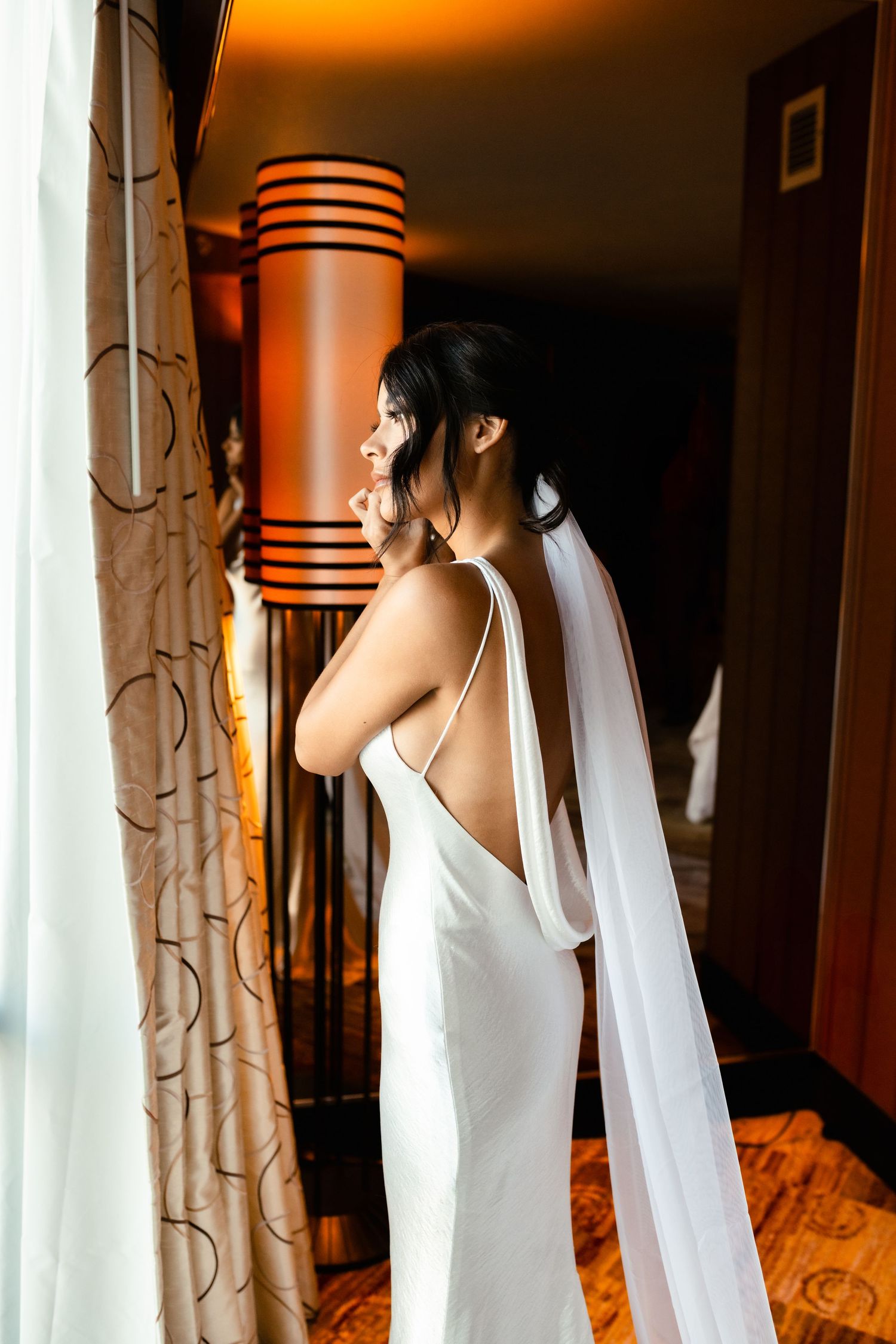 White wedding dress with flowing veil photographed in warm-lit interior setting.