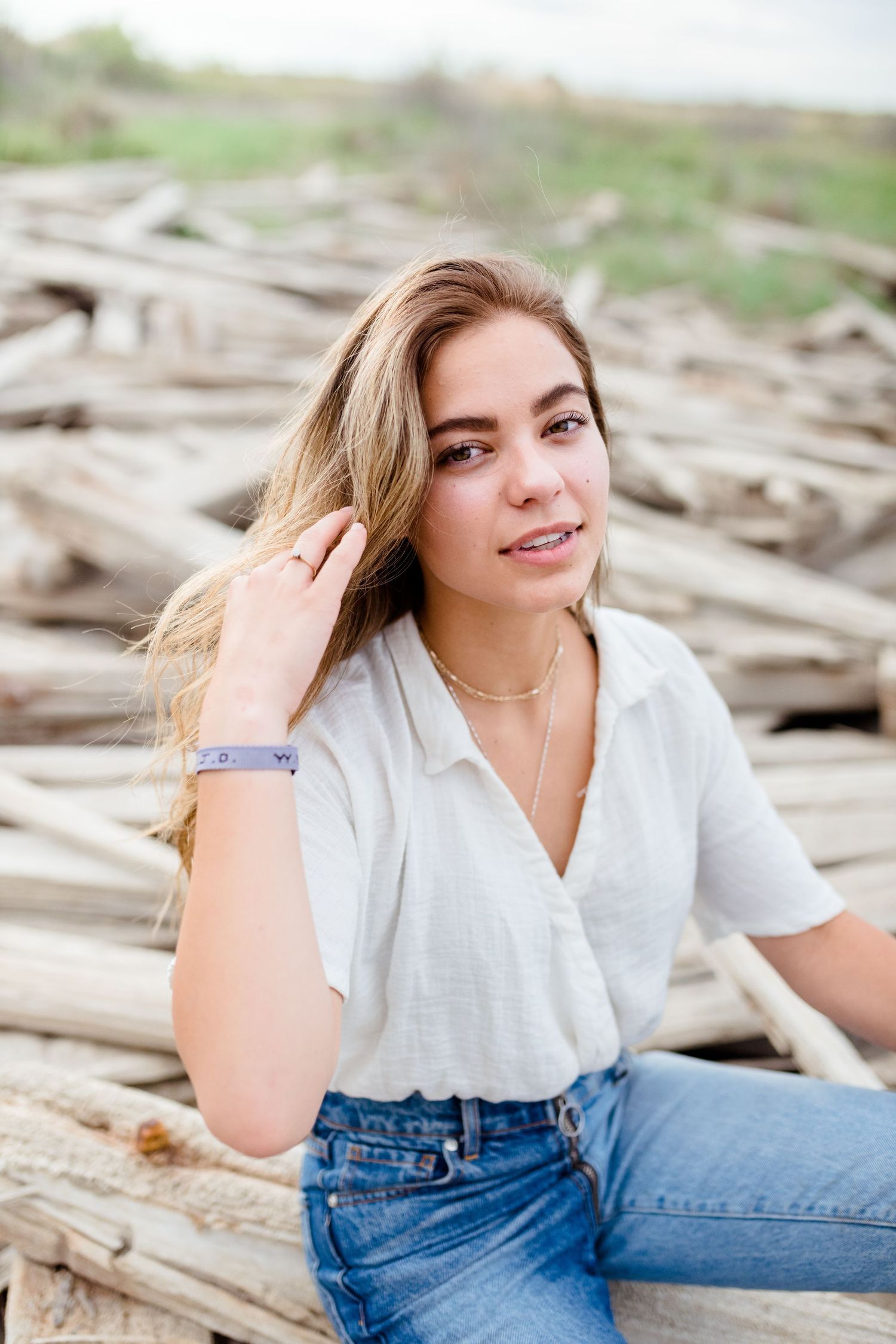Casual outdoor portrait session on driftwood at the beach in blue jeans and white top.