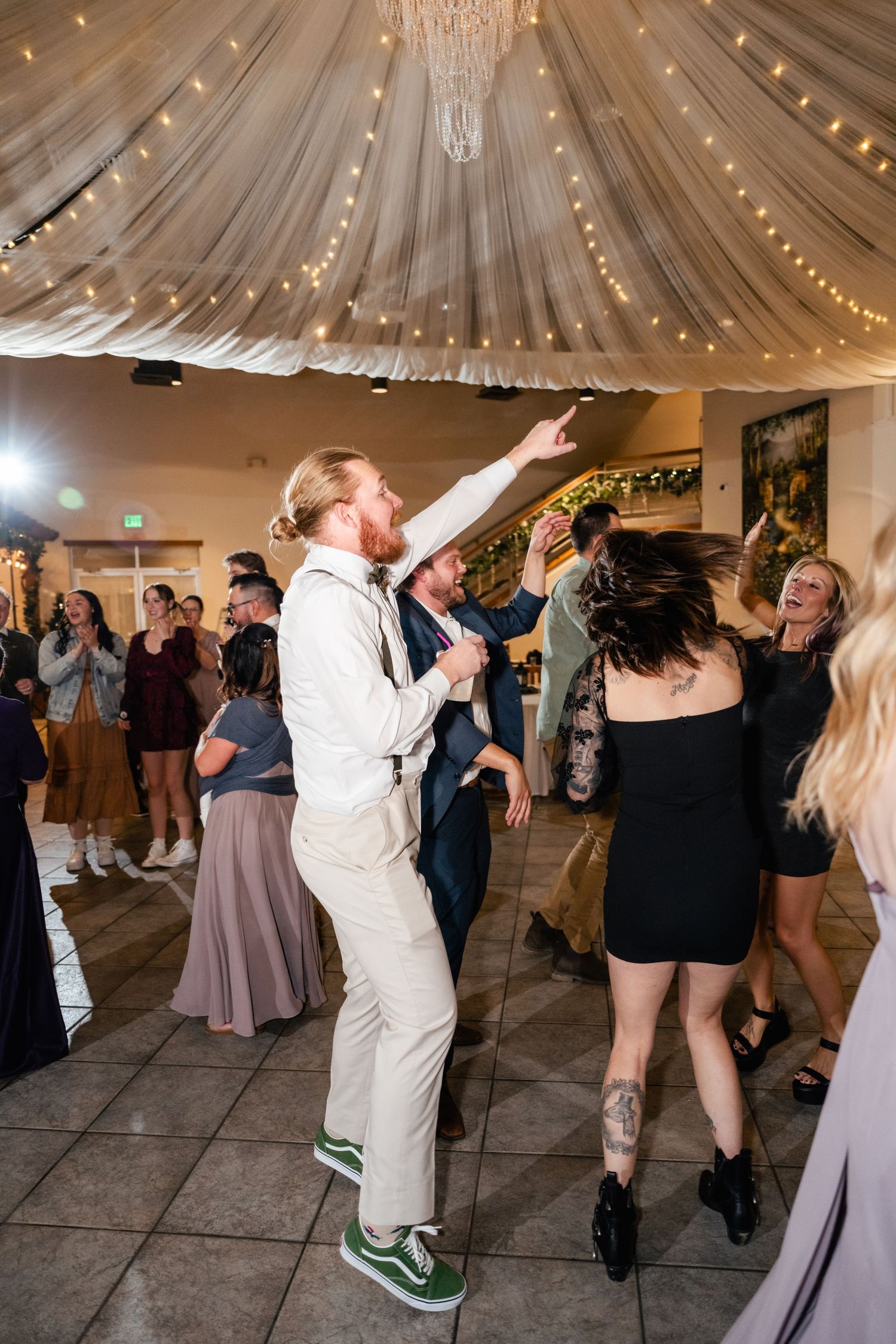 Wedding reception guests dance under a draped ceiling decorated with sparkling string lights.