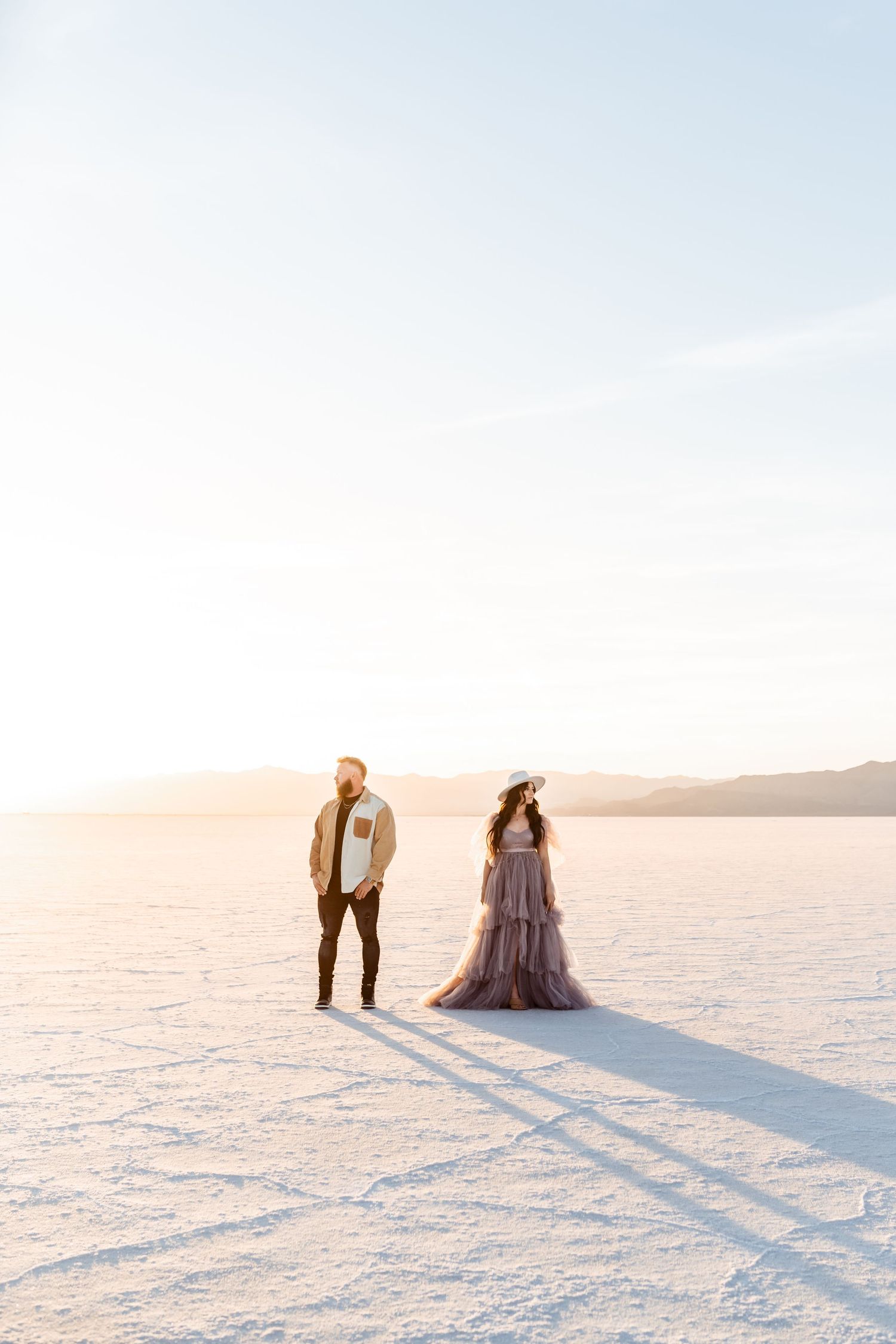 Couple stands back to back holding hands at the Salt Flats by Utah engagement photographer