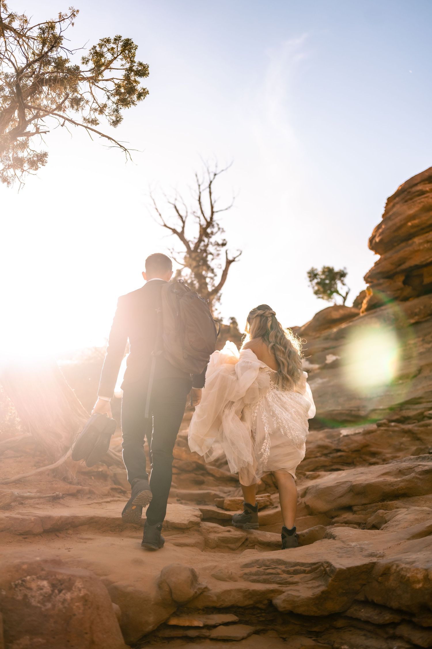 Newlyweds climbing rocky terrain during golden hour photography session.