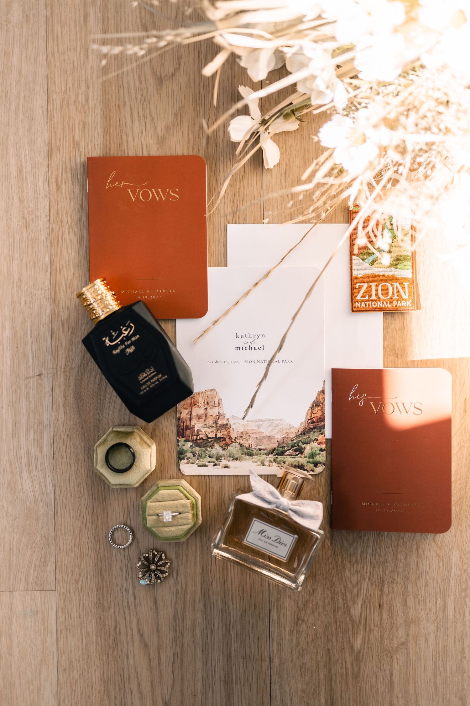Wedding details flatlay with vow books, perfume bottle and Zion National Park elements.