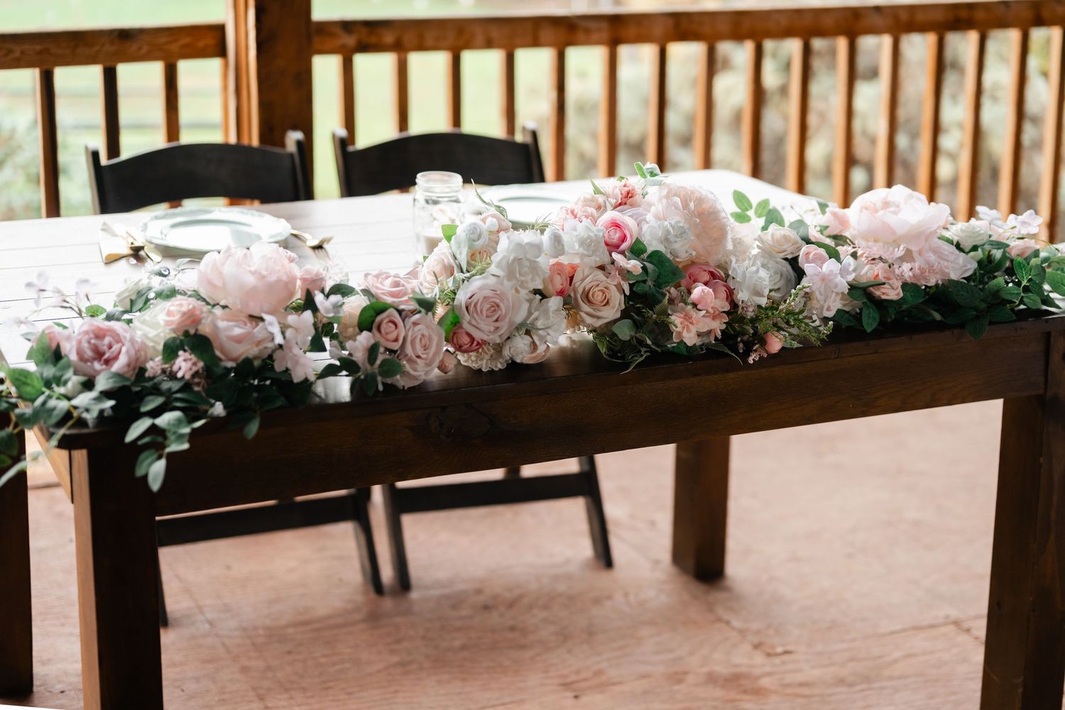 Long floral garland with pink and white roses decorating a wooden railing at an outdoor venue.