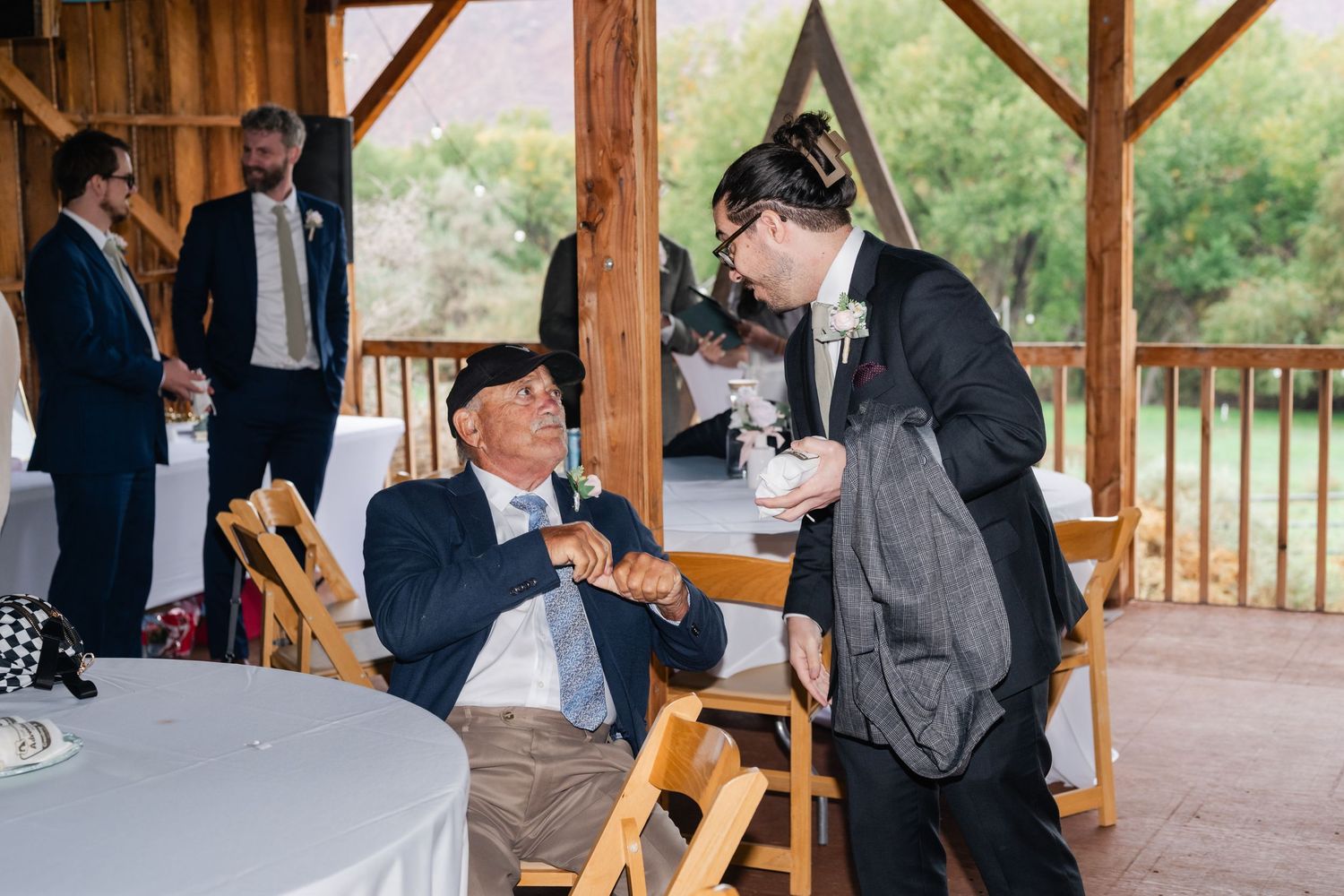 Guests celebrating at a rustic outdoor wedding venue with wooden beams and natural lighting.