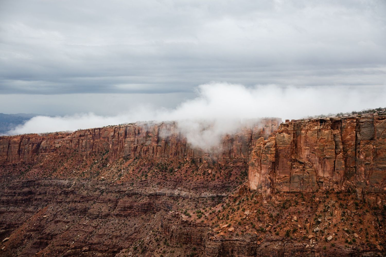 Panoramic view of red rock cliffs and canyons with dramatic cloudy skies in the desert landscape.