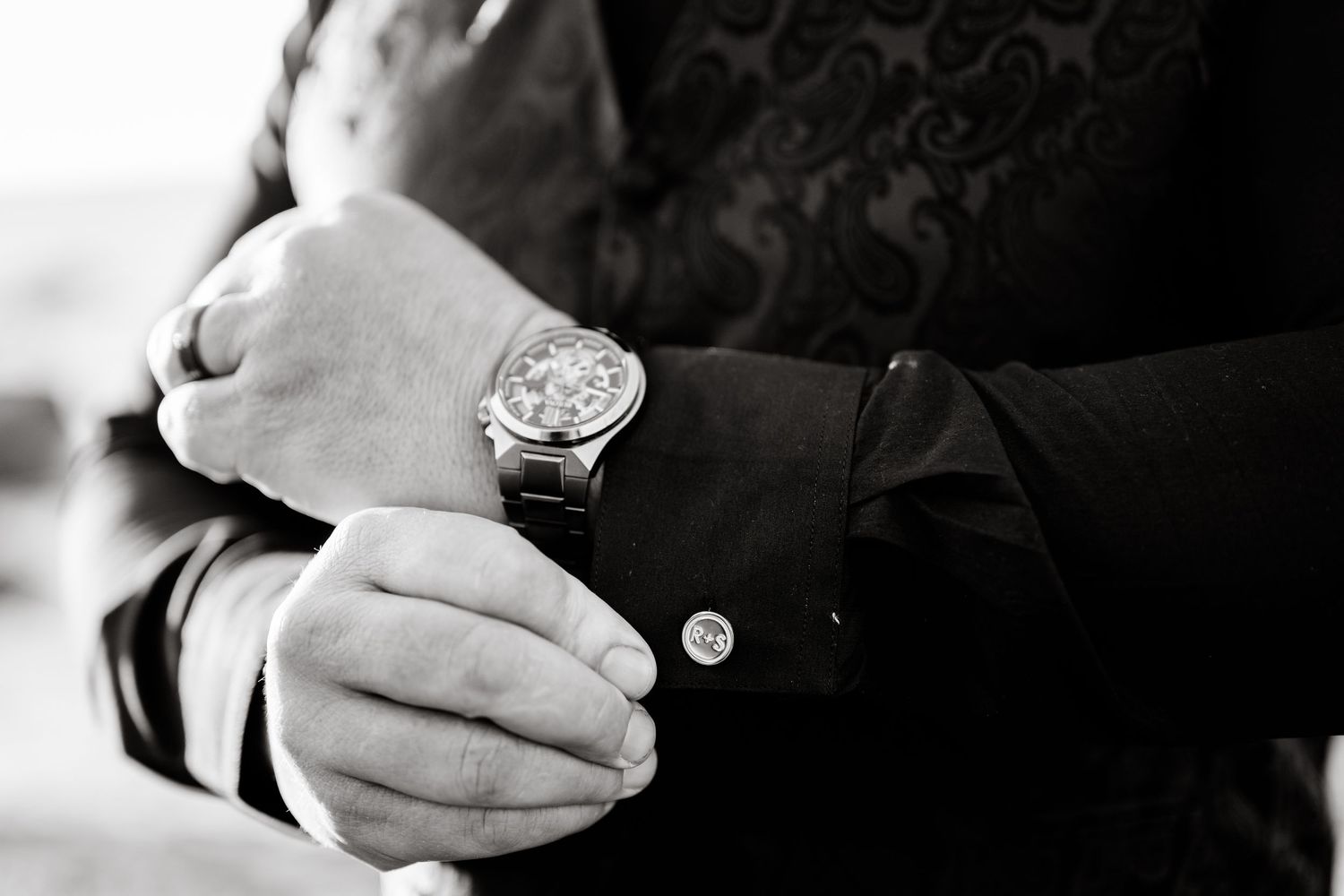 Close-up detail shot of a luxury watch and formal attire cuff buttons in black and white.