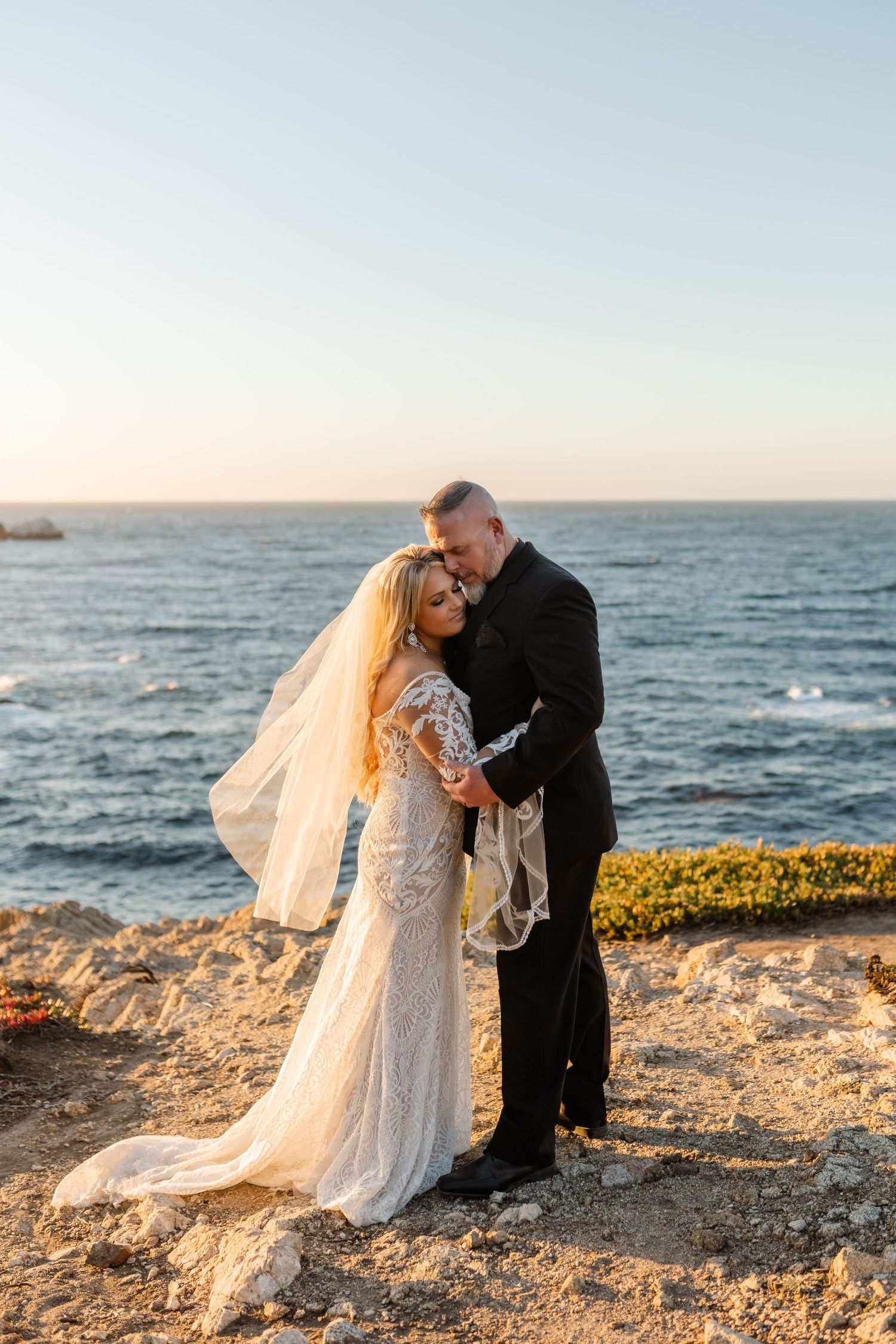 A romantic coastal wedding portrait with ocean waves and golden sunset light.