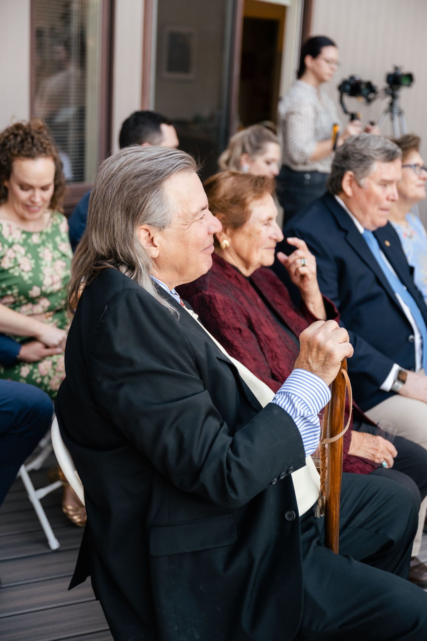 Wedding guests seated in formal attire watching ceremony on outdoor deck.