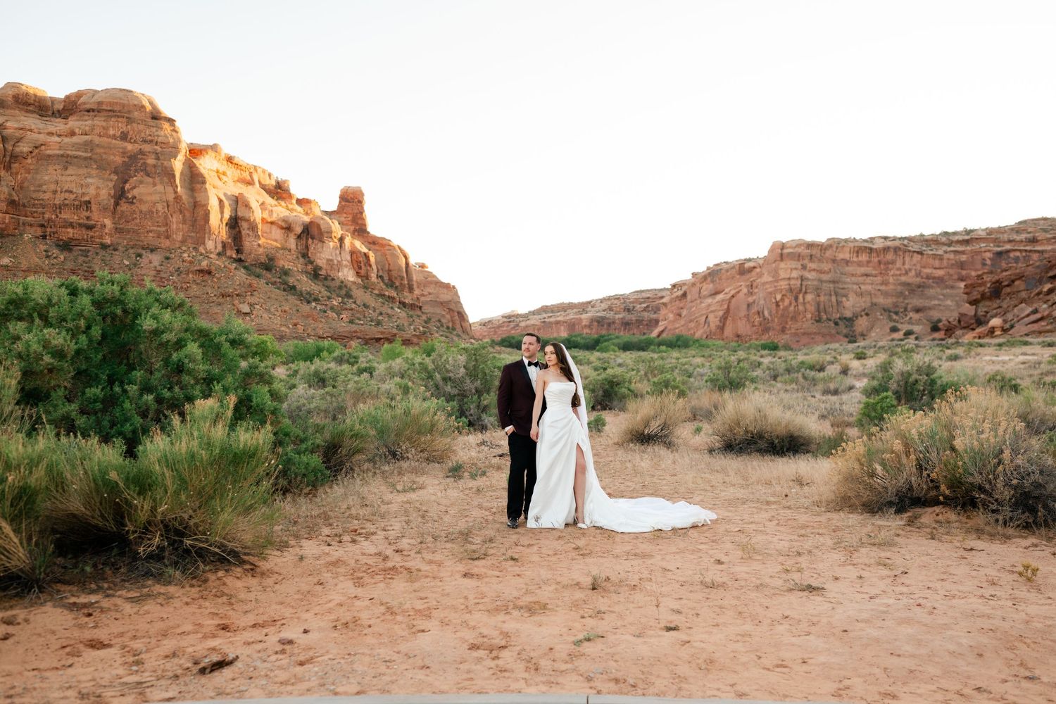 Bride and groom embrace in a stunning red rock desert canyon landscape during their outdoor wedding ceremony.