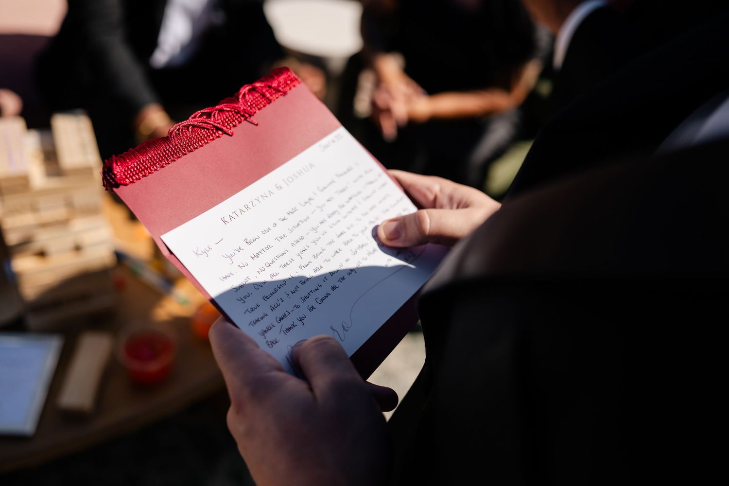 Person holding a red and white wedding program card with handwritten notes at an outdoor reception event.