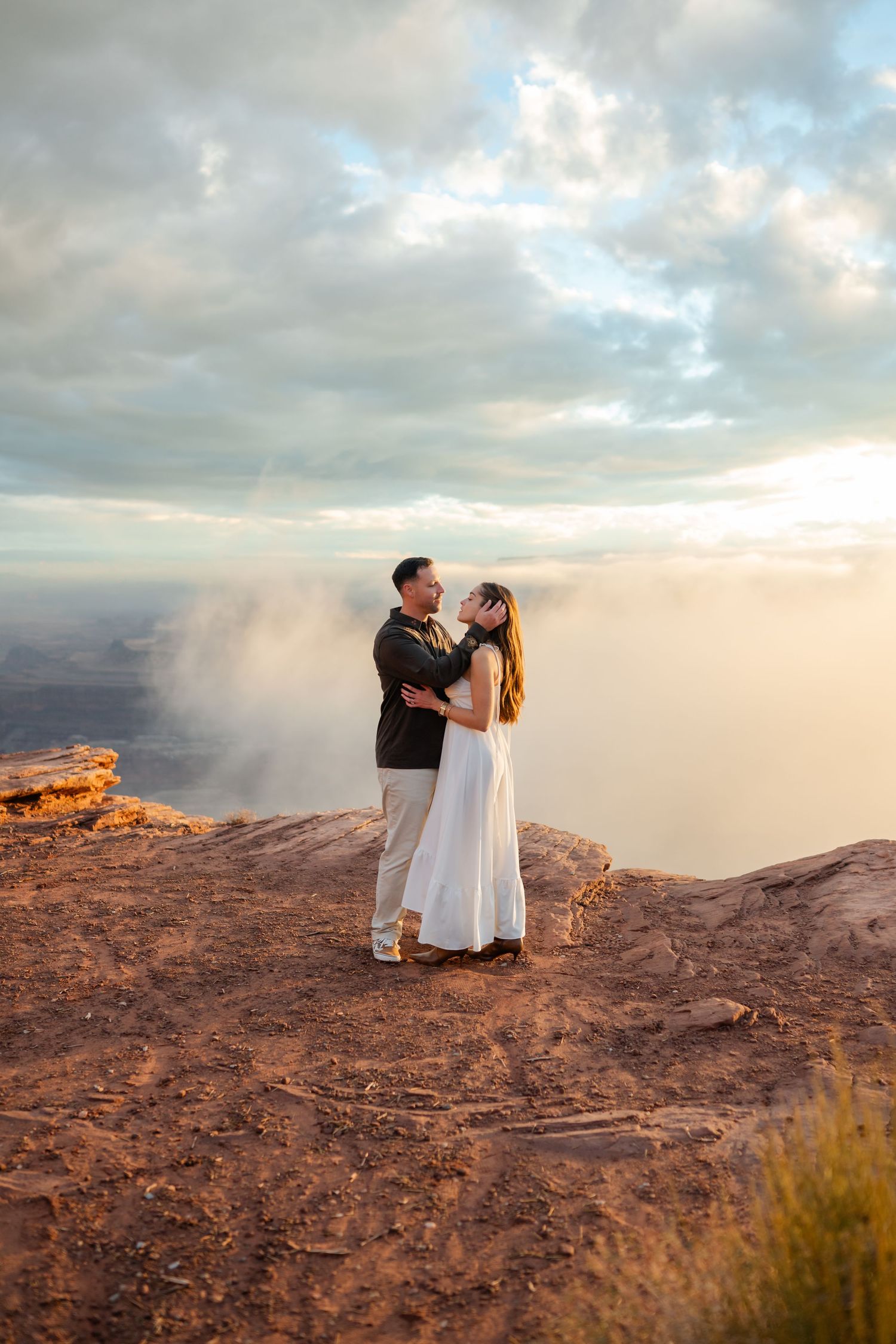 A couple shares a romantic moment at sunset on a scenic desert cliff overlooking a vast canyon vista.