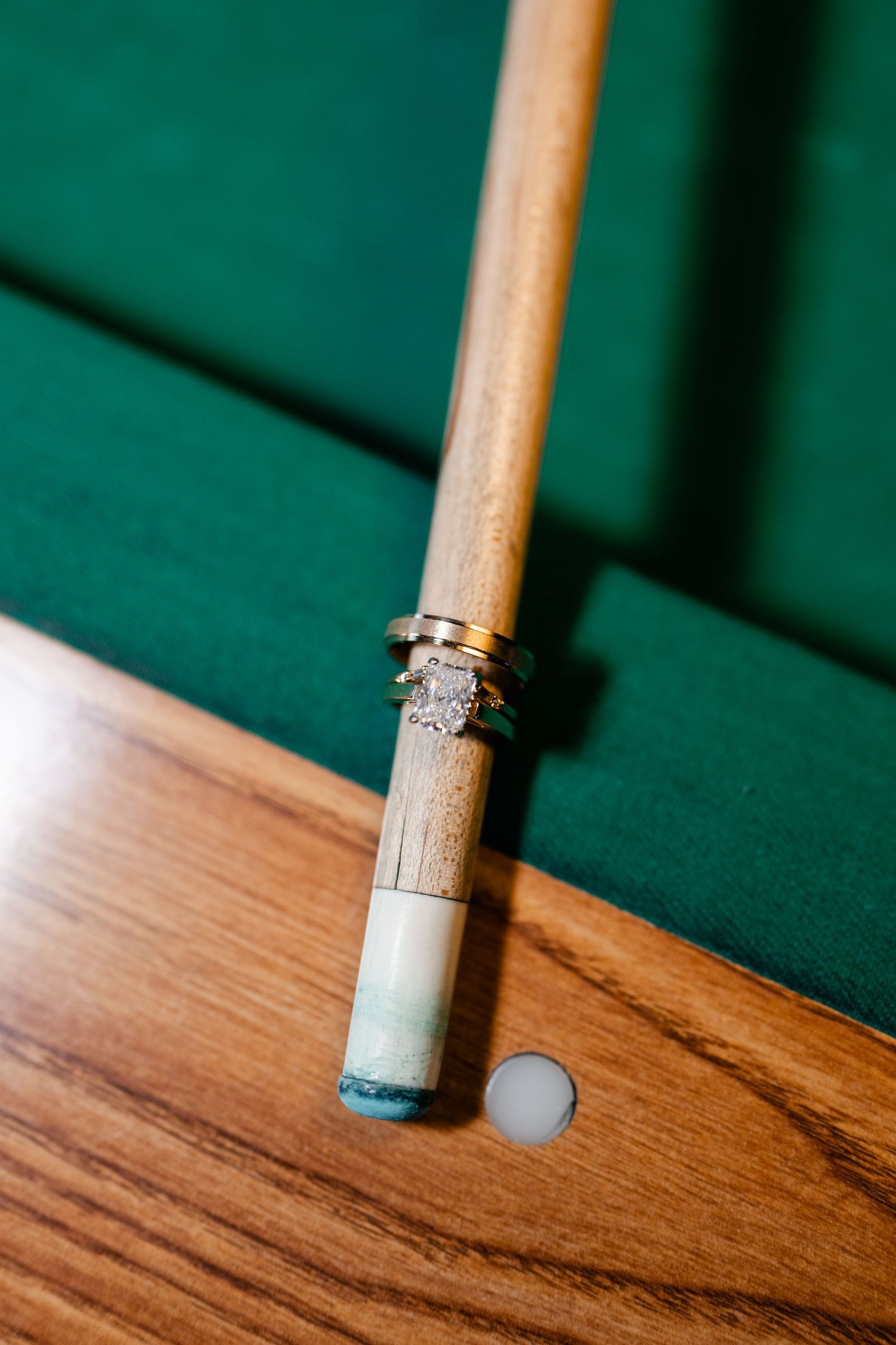 Wedding rings displayed creatively on a wooden pool cue against green felt background.