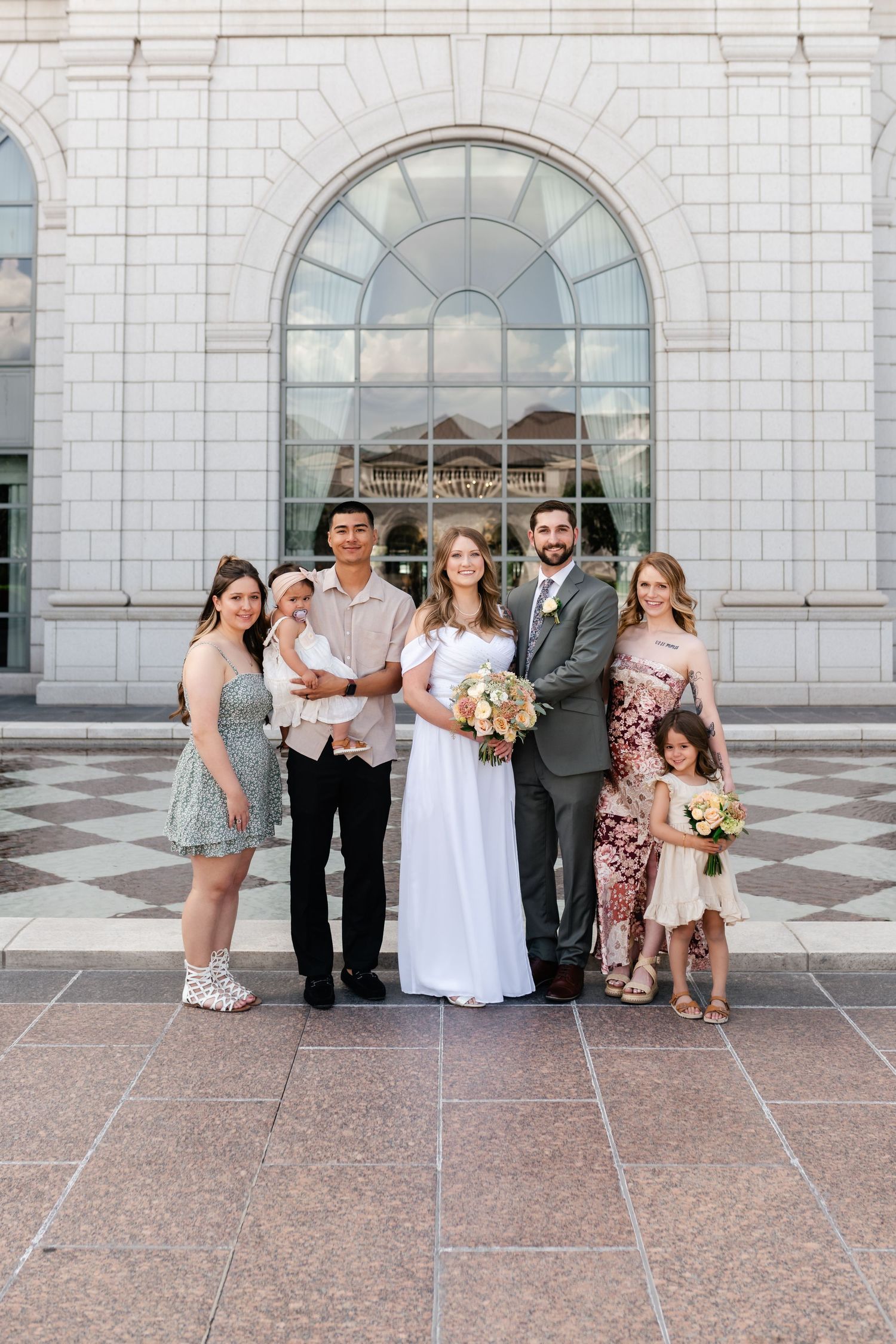 Wedding party poses in front of a grand white stone building with arched windows.