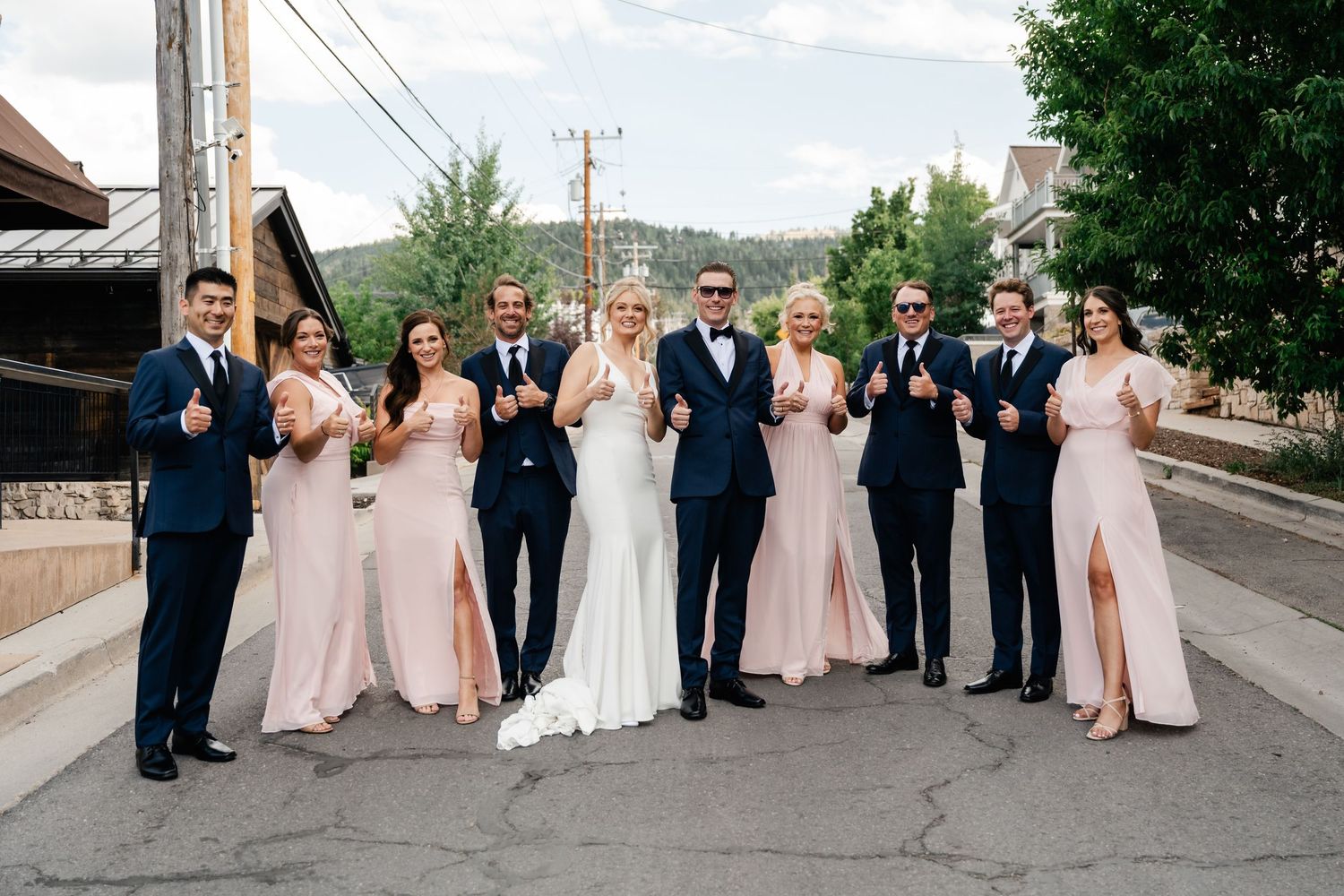 Wedding party members walking in a line along a residential street wearing pink dresses and dark suits.