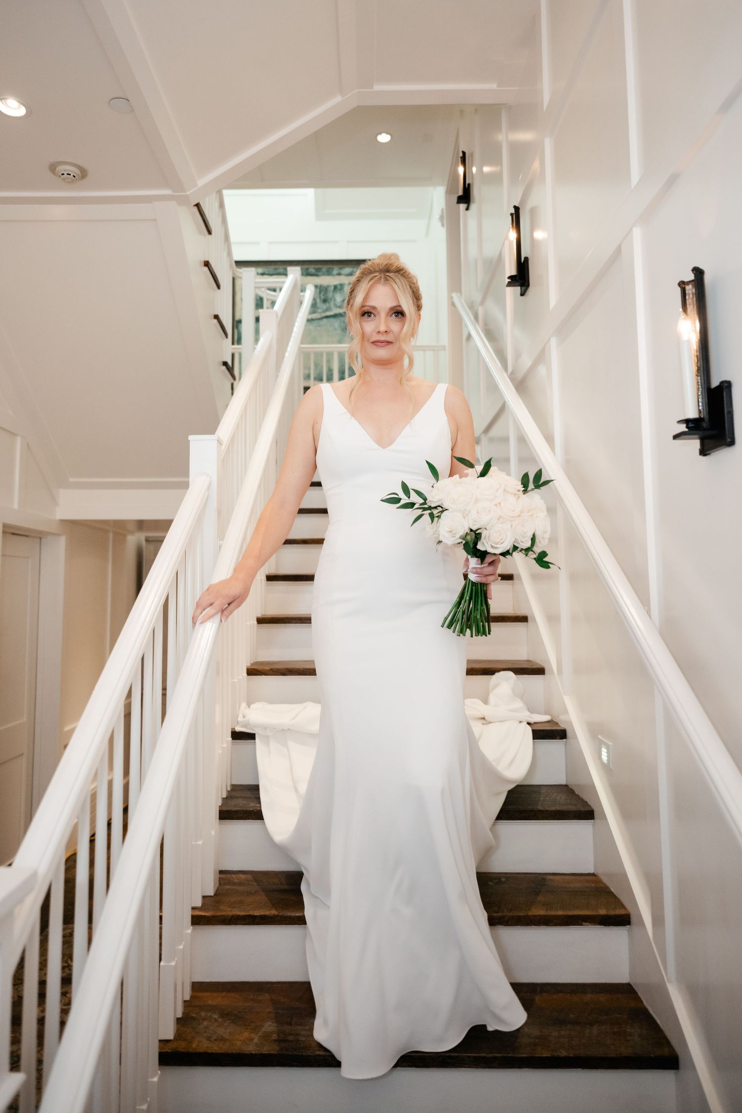 Bride in white gown descending elegant white staircase in sequence of wedding day photos.