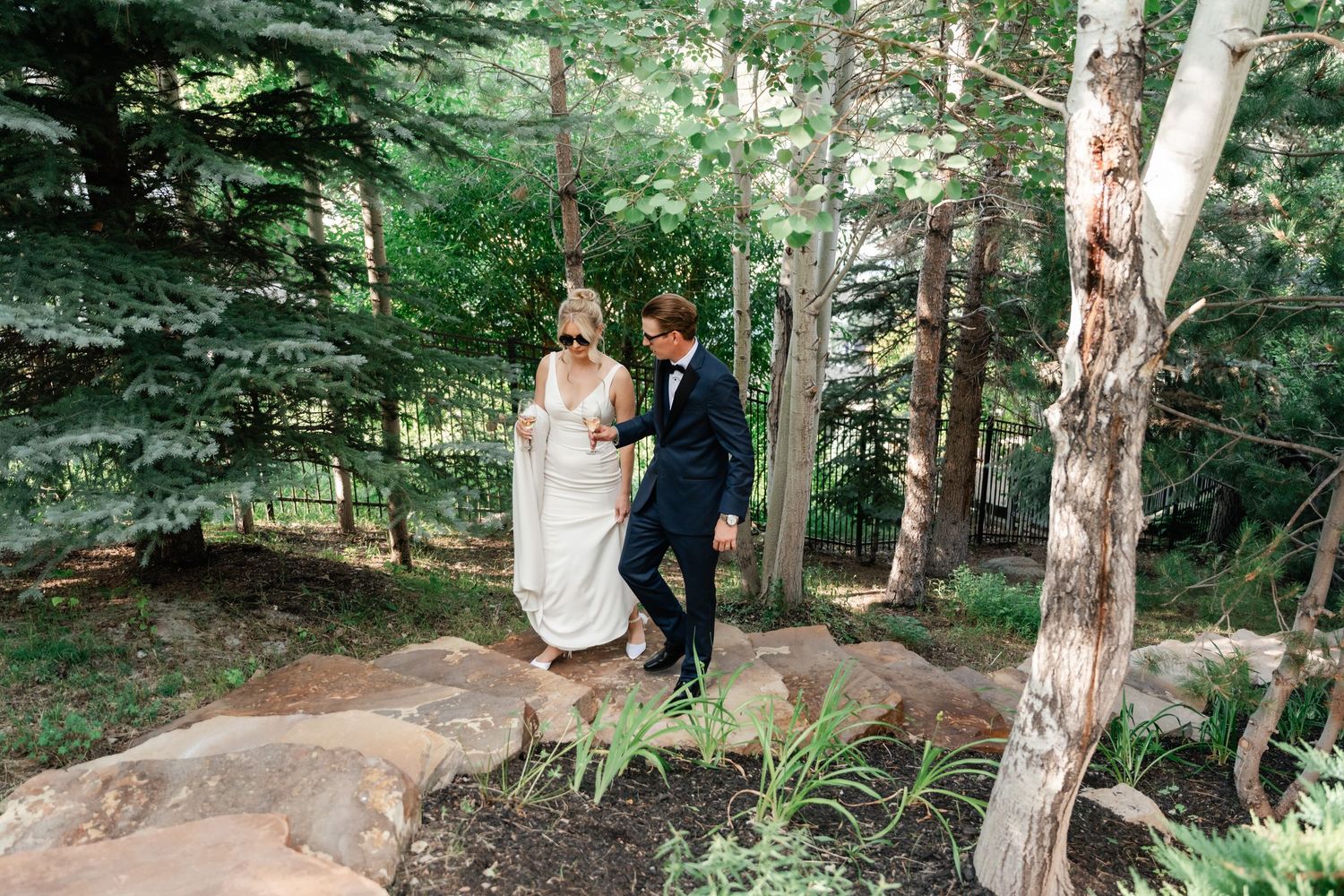 Wedding couple stands playfully on rocky terrain surrounded by forest trees.