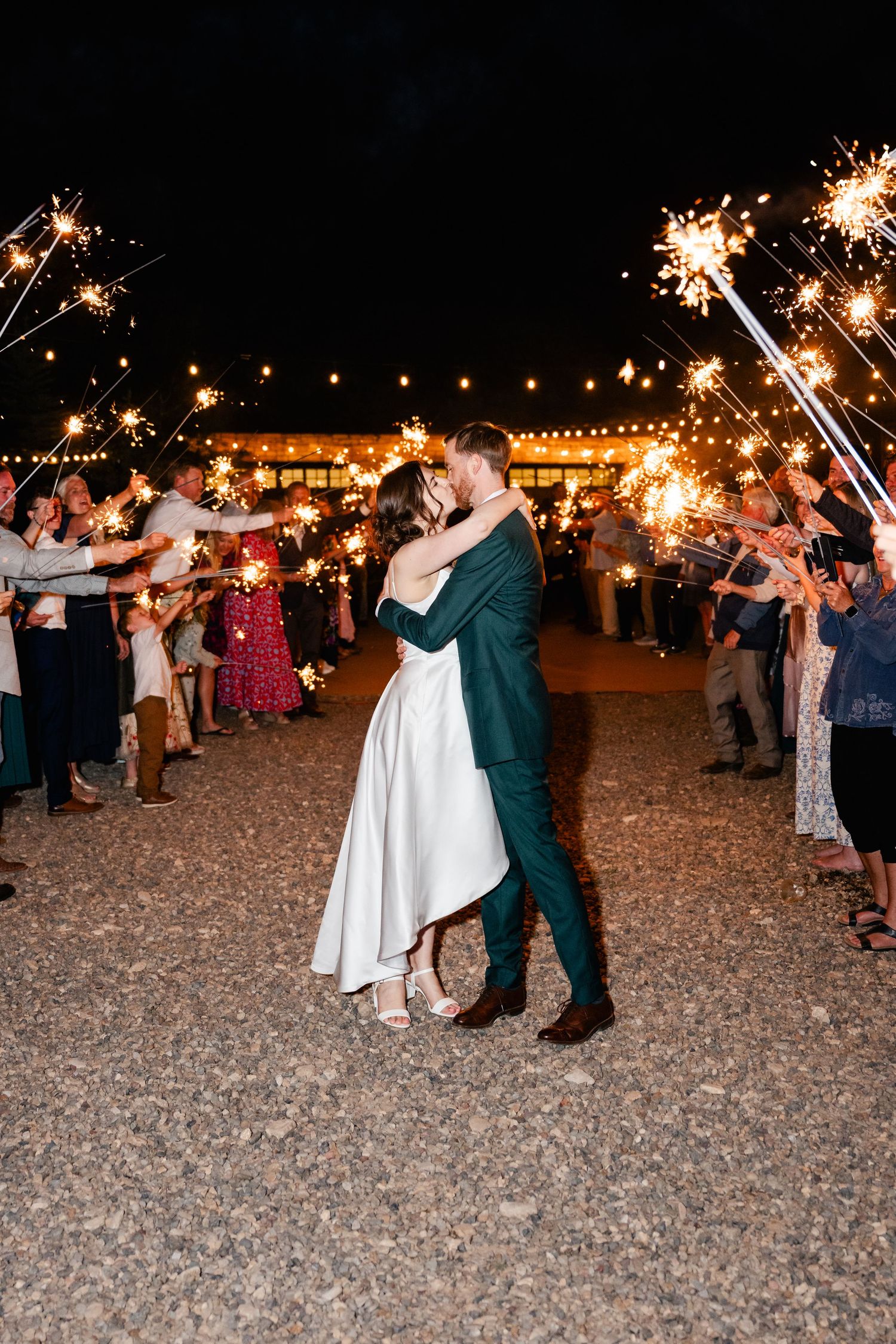 A couple shares a romantic dance moment under sparklers and string lights at an outdoor evening celebration.