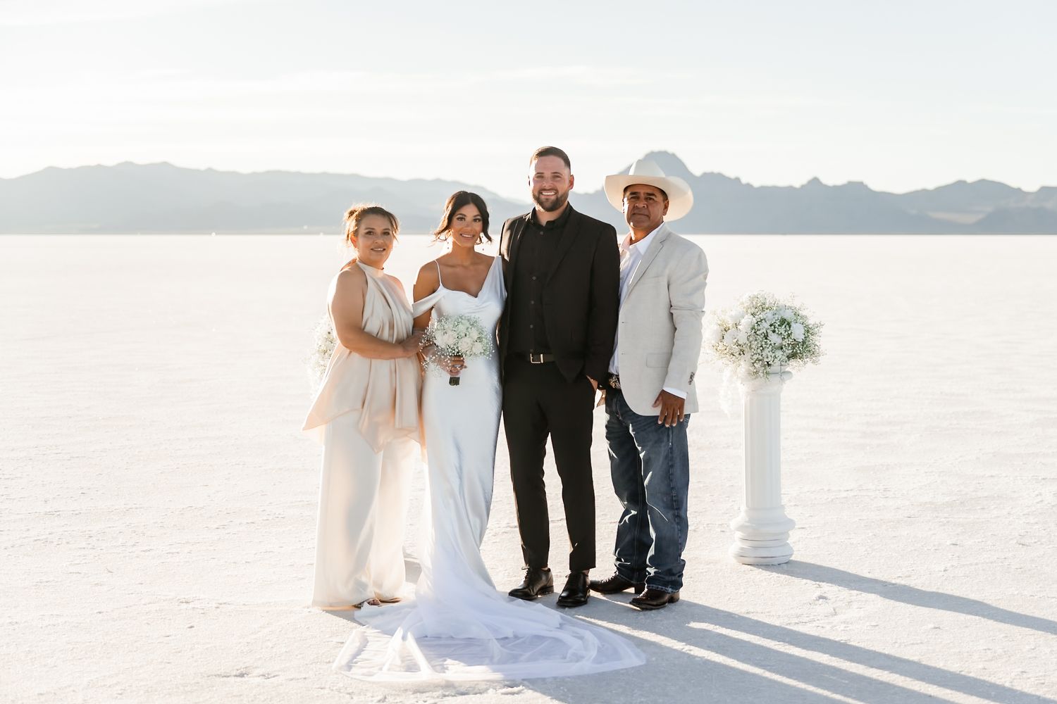 Wedding party posing for photos on white salt flats with mountains in the distance.