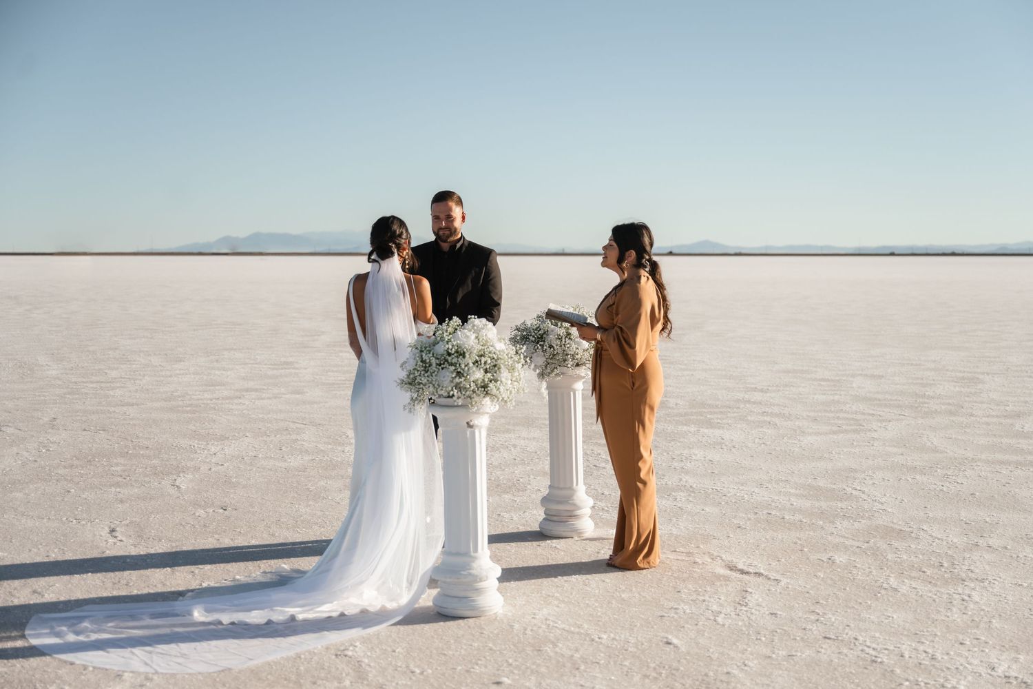 Wedding ceremony setup on white salt flats with mountains in background.