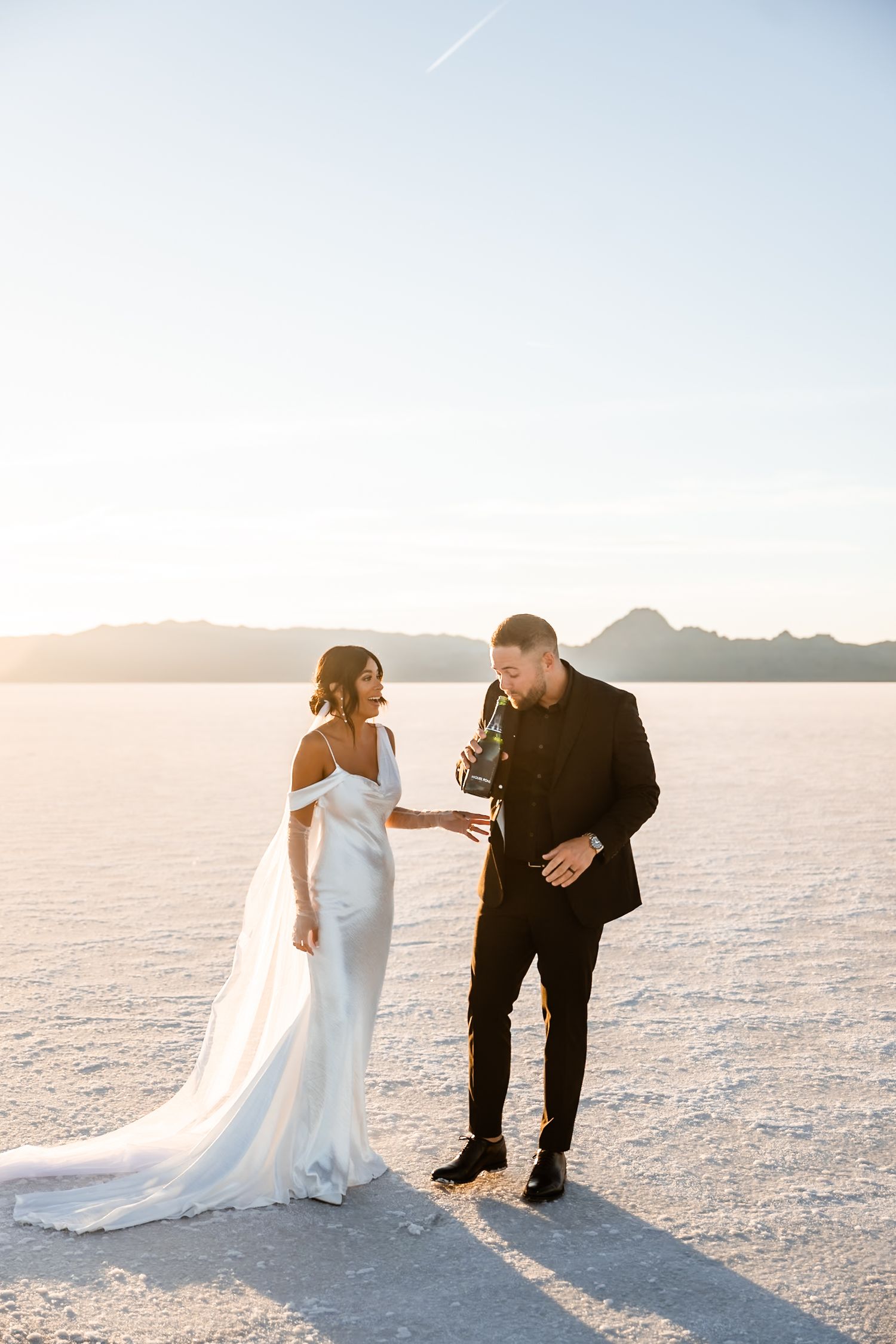 A wedding couple shares a moment on salt flats with mountains and sunset in background.