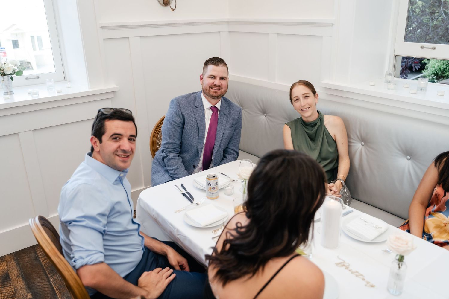 Wedding party members seated at tables during an intimate indoor reception celebration.