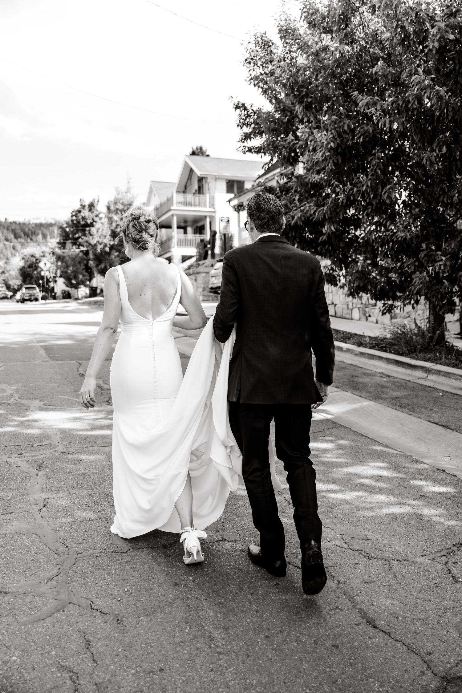 A bride and groom walk together down a sunlit street on their wedding day.