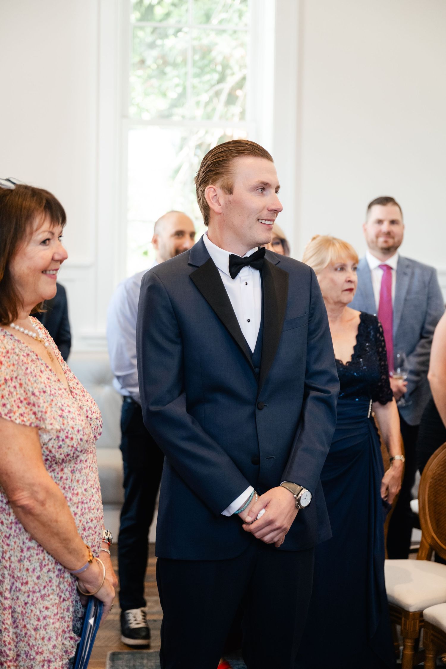 Wedding guests gathered in a bright room with white walls and chandelier.