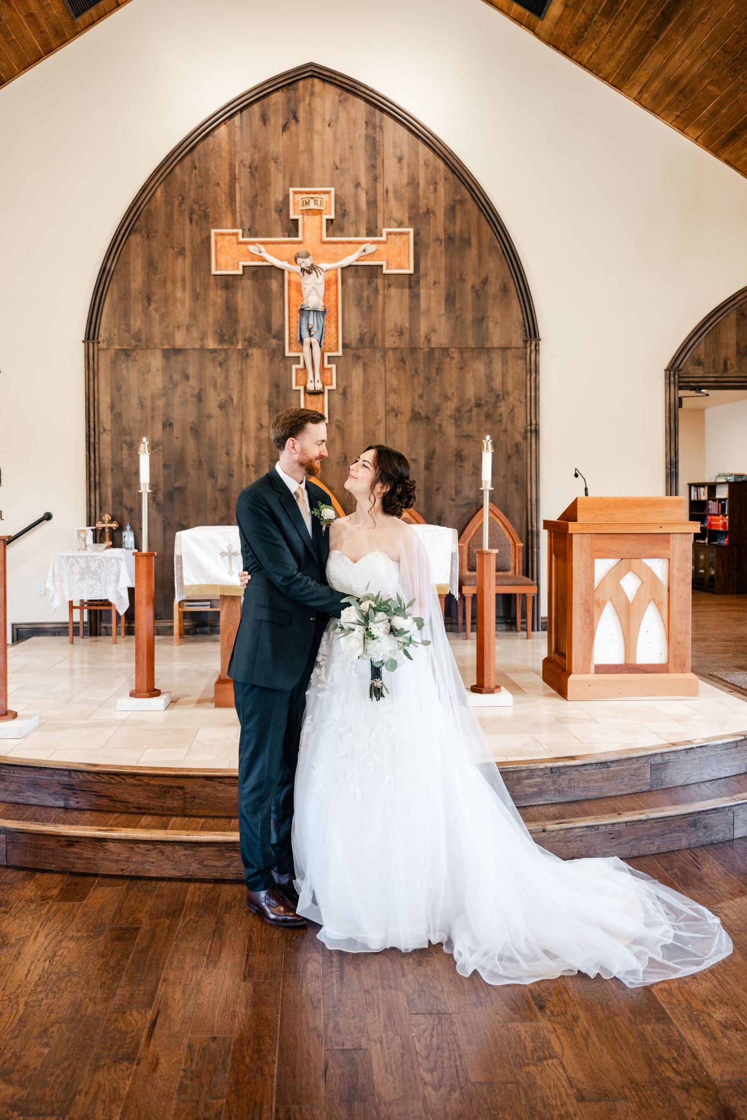 A romantic first look sequence between newlyweds in a rustic wooden chapel with a cross on the wall.