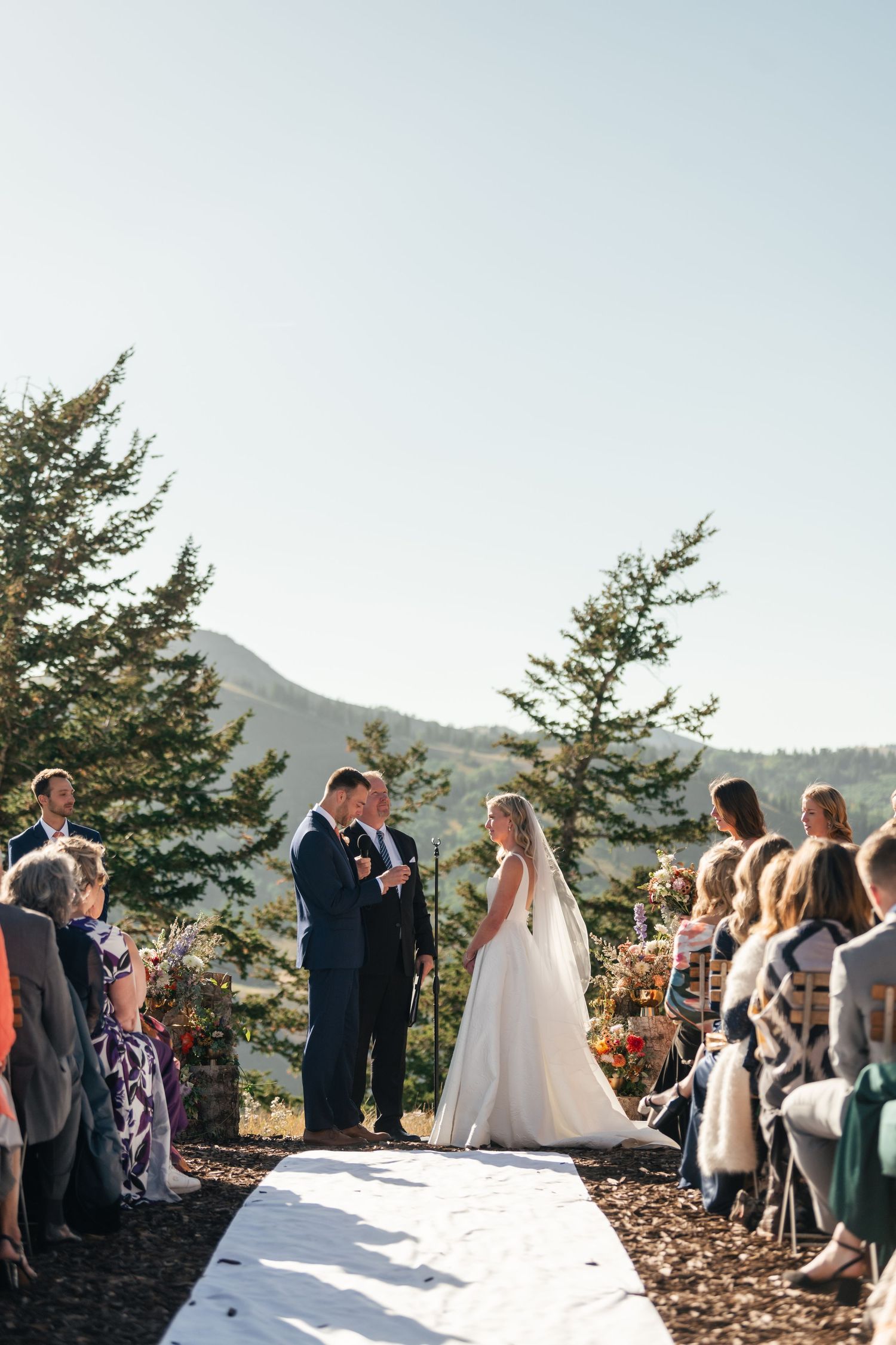 Outdoor mountain wedding ceremony with guests seated on both sides of white aisle runner.