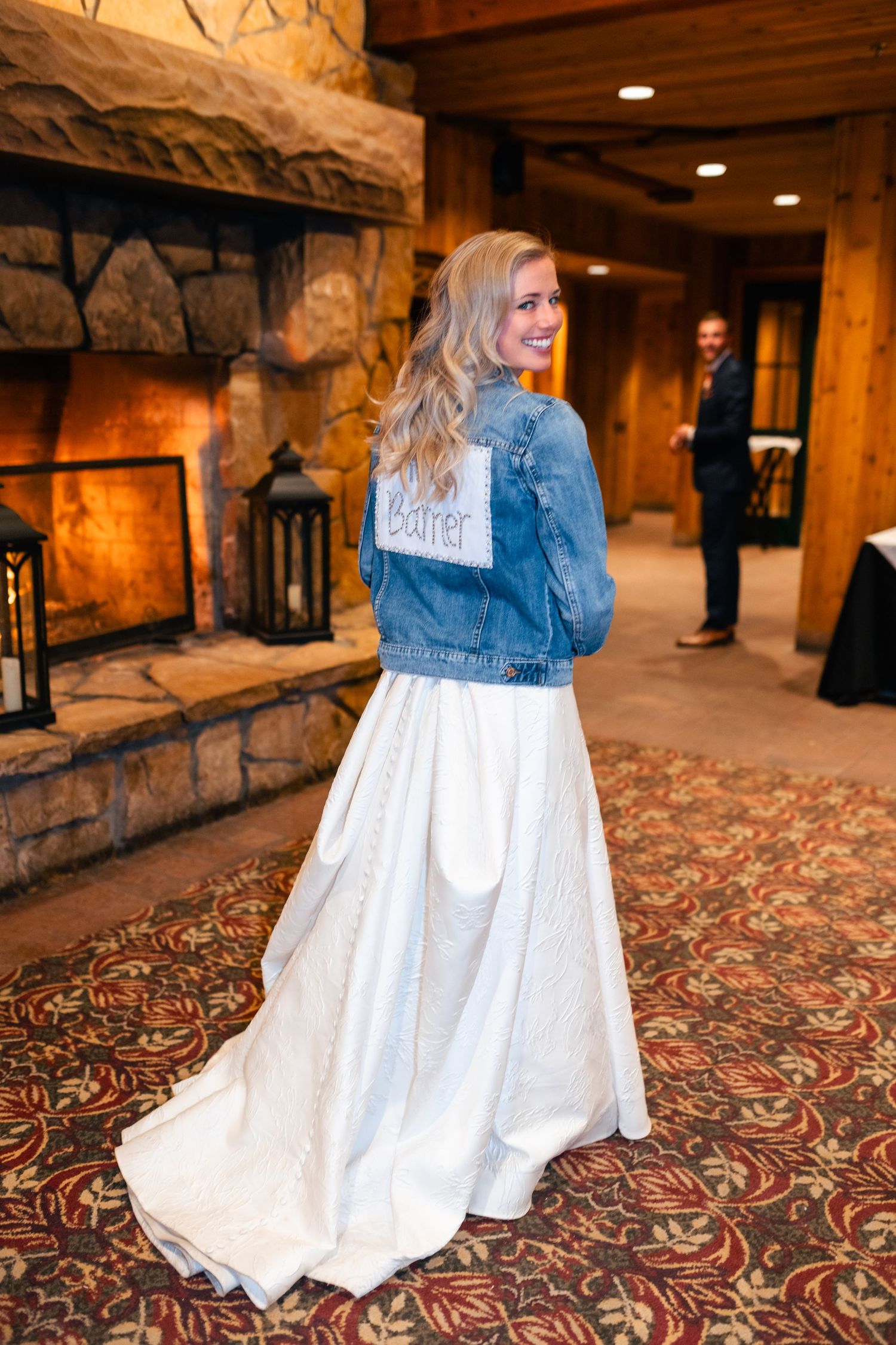 A bride in a white wedding dress paired with a casual denim jacket walks through an elegant venue.