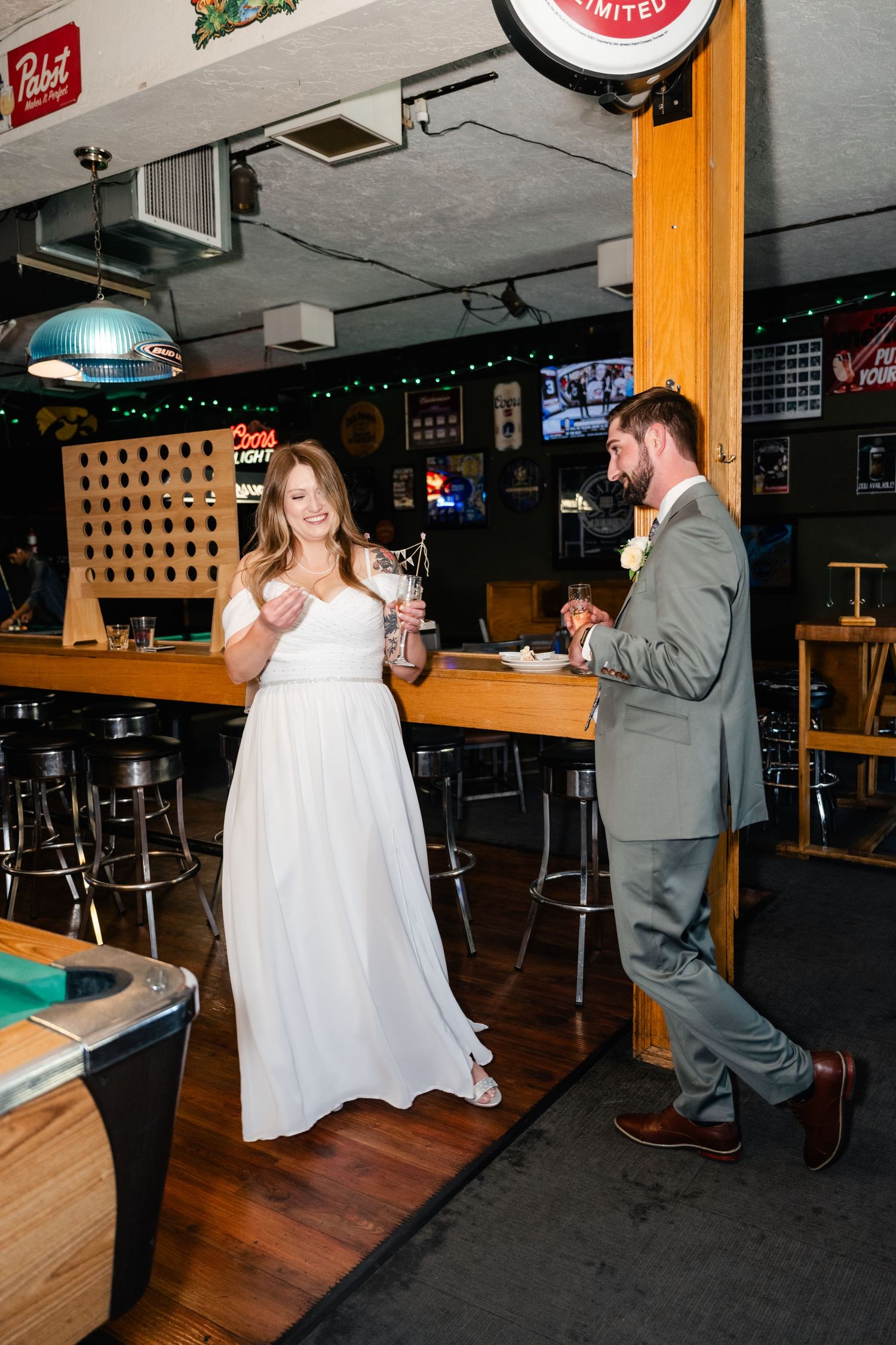 A couple in formal attire enjoys drinks at a casual bar with a pool table.