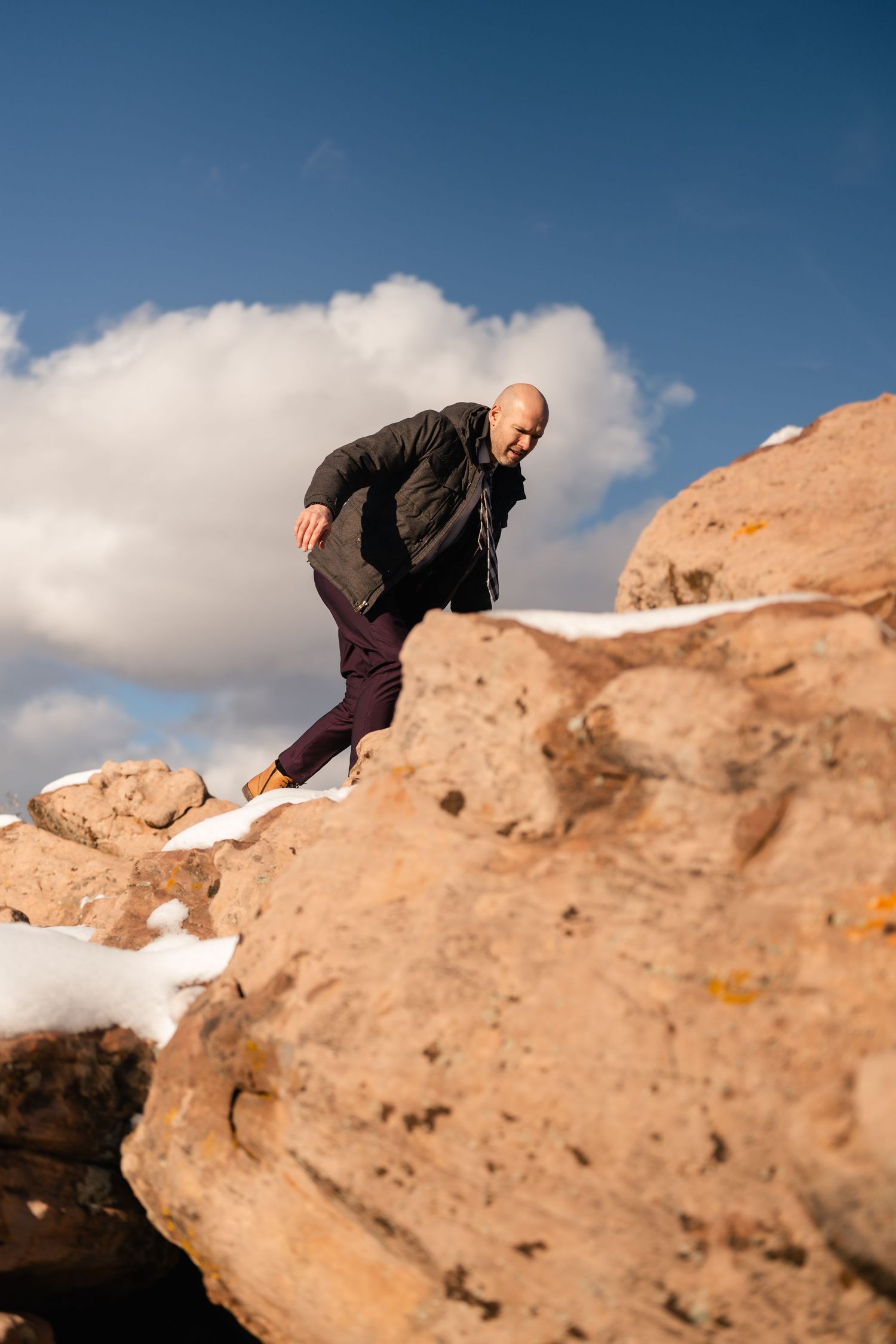 Person climbing on red sandstone rocks against a bright blue desert sky.