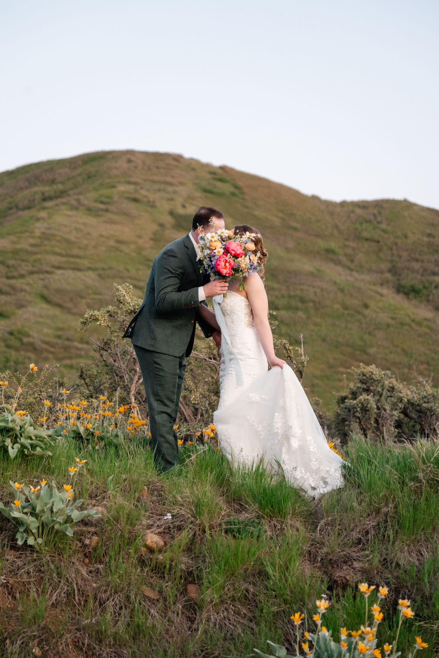 Romantic wedding portraits taken among yellow wildflowers on mountainside during golden hour.