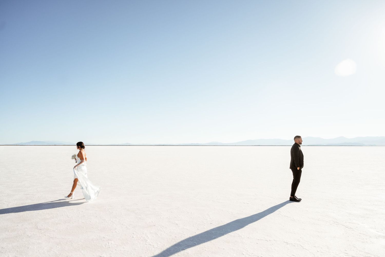 Minimalist wedding photography on salt flats with distant mountains and blue sky.