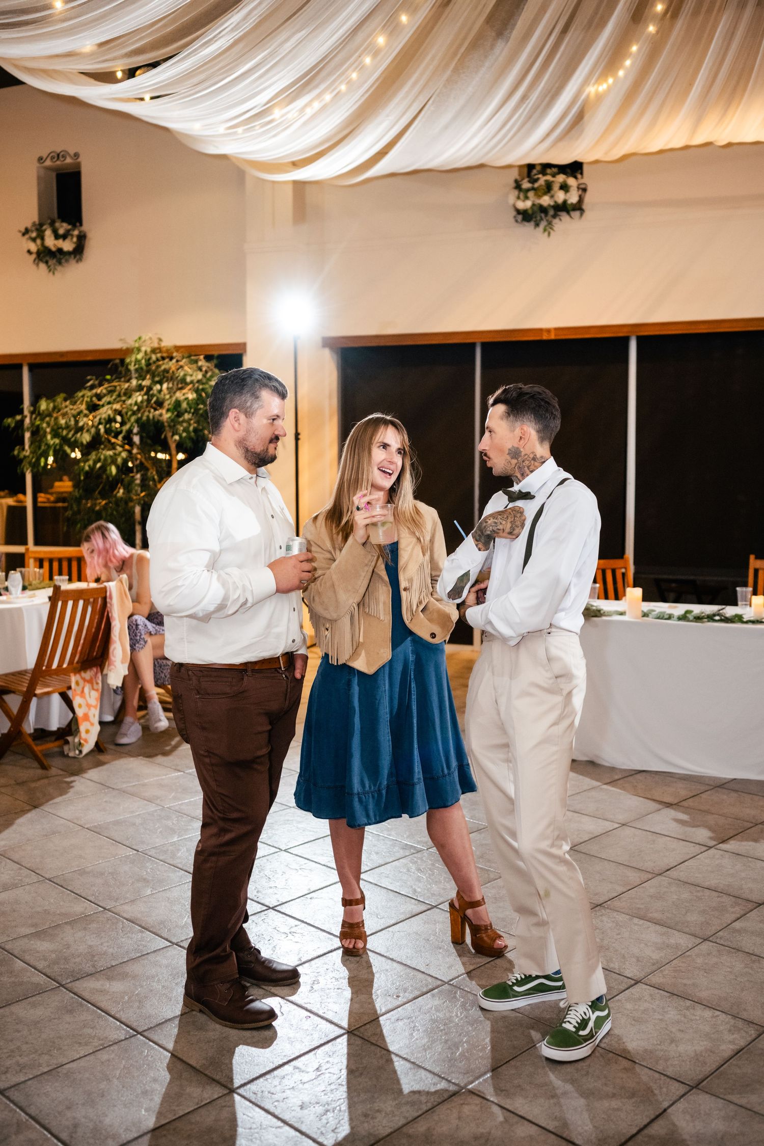 Guests in casual formal attire enjoying conversation at an indoor event with draped fabric decor and tiled floors.
