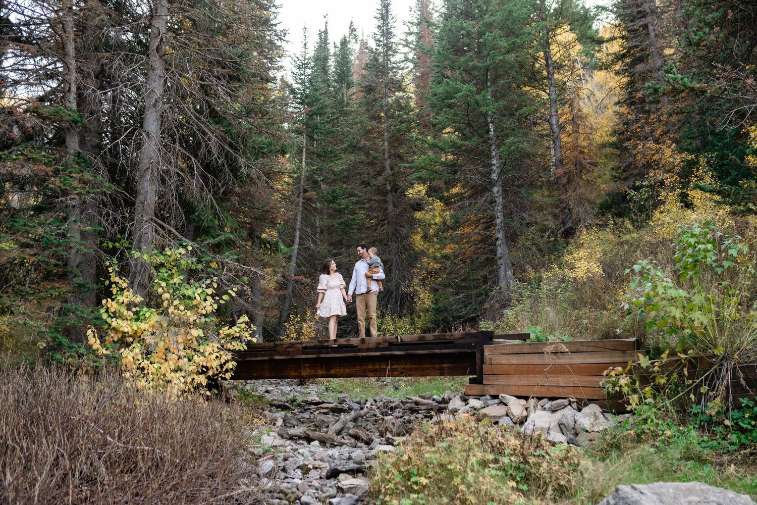 Family standing on a bridge over a creek during their fall family session by Coley Cook Photography