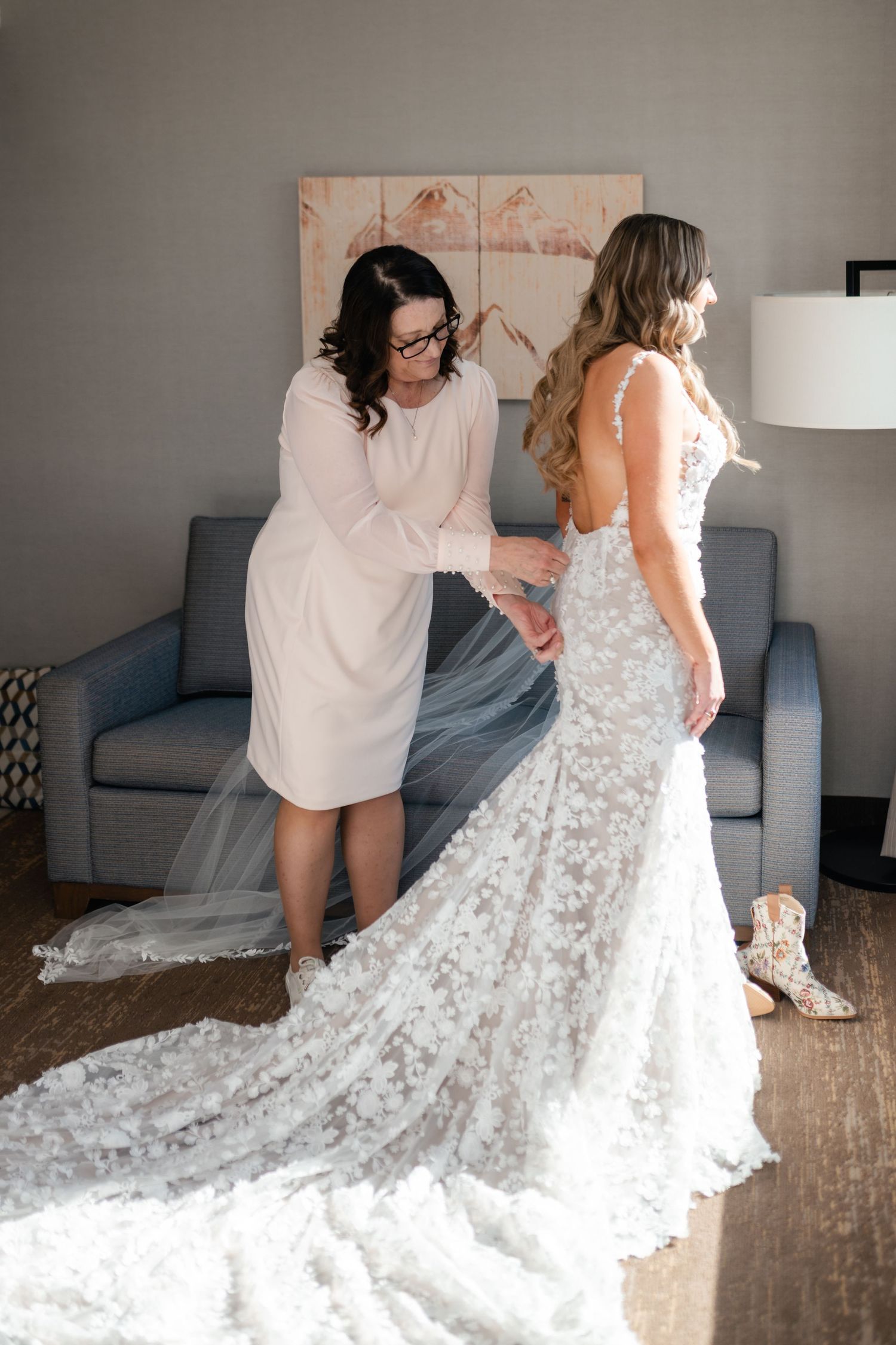 A bride in a stunning lace wedding gown with long train gets help with final adjustments before her ceremony.
